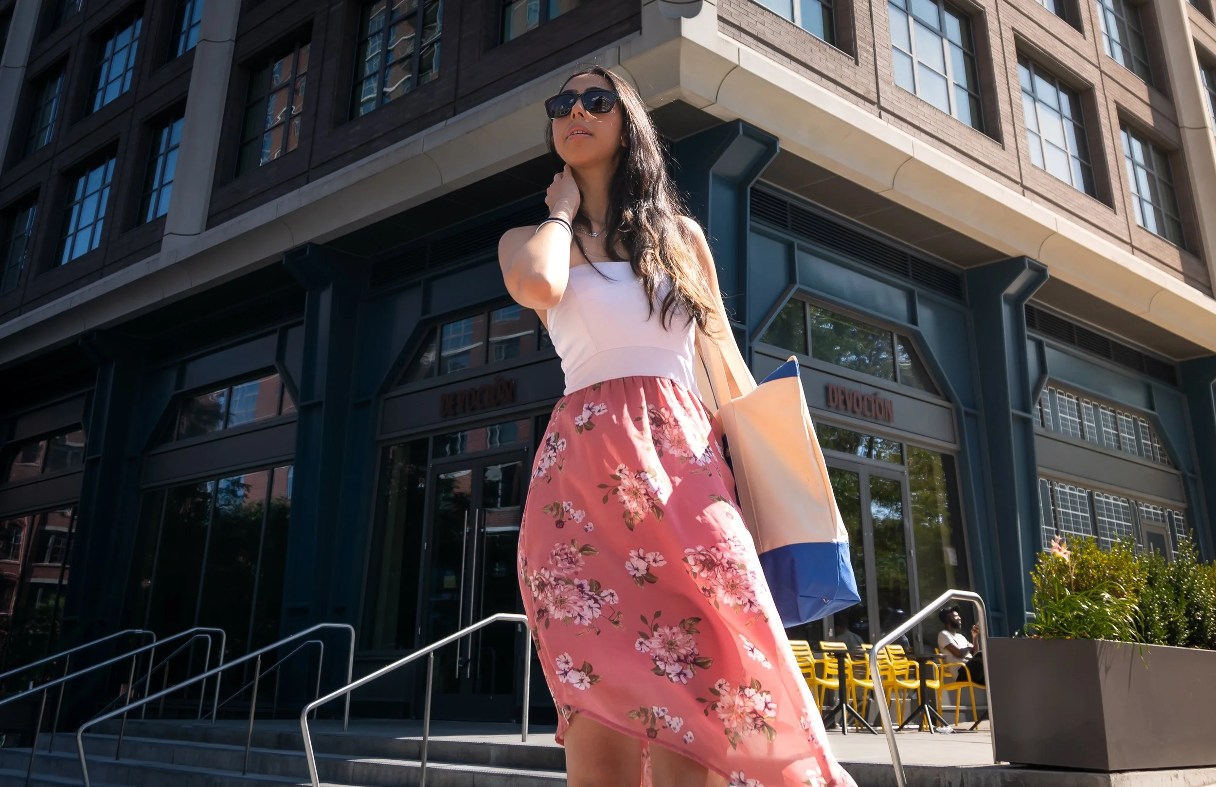 Editorial fashion portrait of Harshita in a floral skirt and sunglasses outside a modern building in Brooklyn