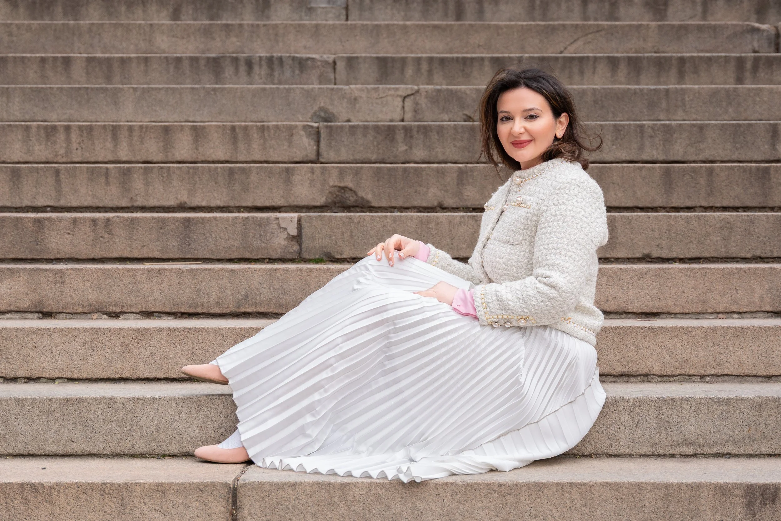 Silvia seated on stone steps in Central Park NYC wearing a white skirt and textured jacket in an editorial fashion portrait