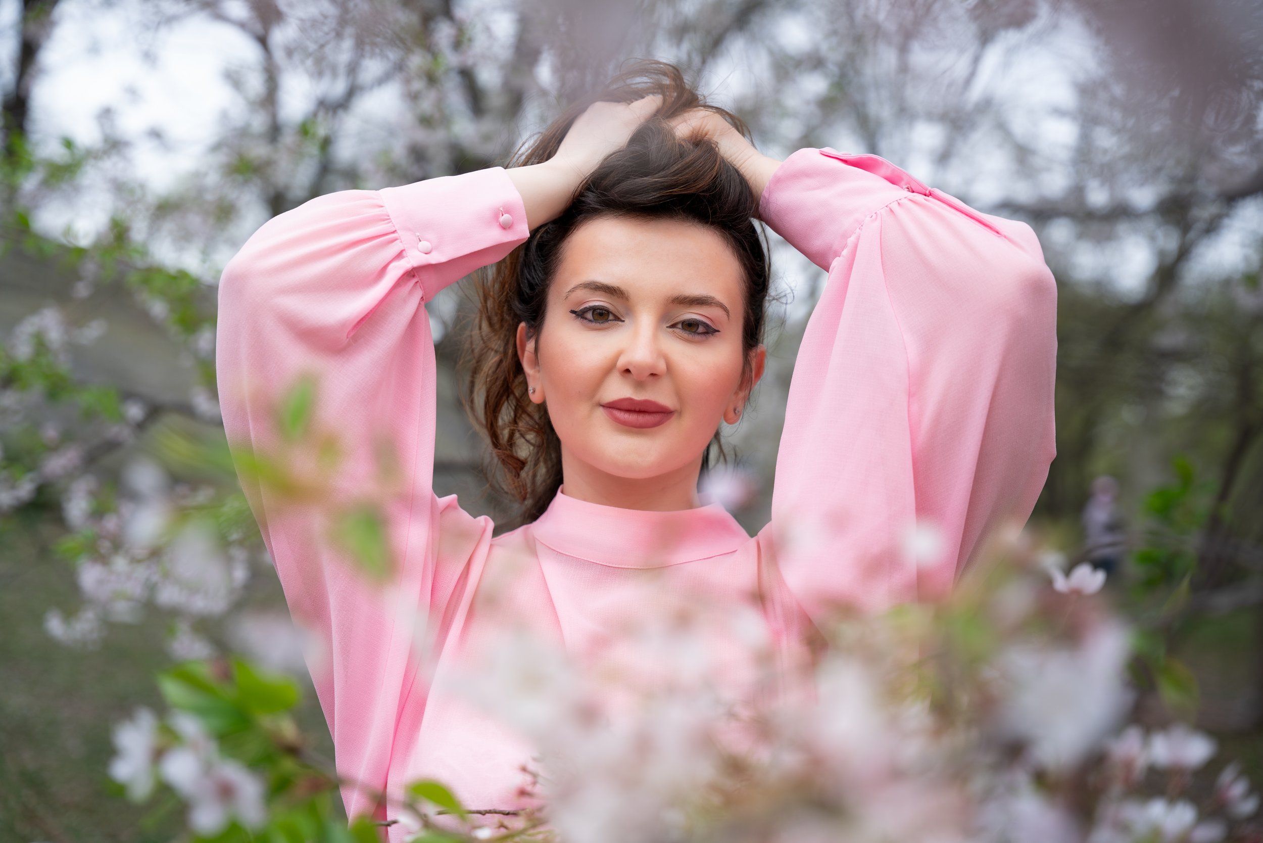 Silvia editorial portrait in Central Park NYC wearing a pink blouse, framed by soft cherry blossoms in natural light