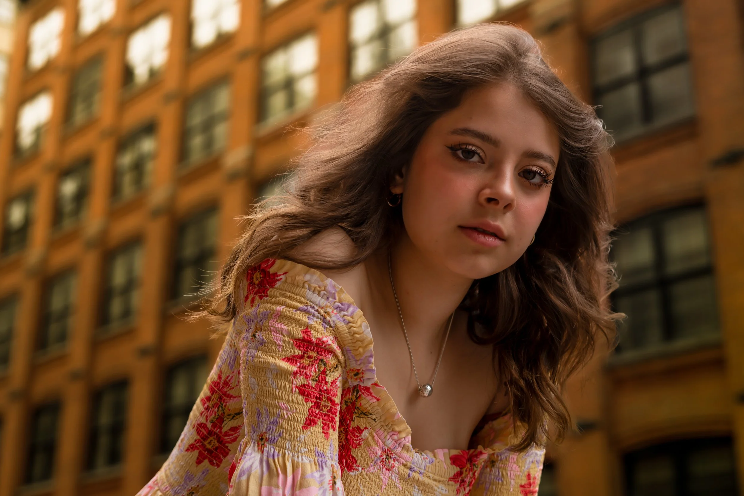 Editorial model portrait of Julianna in a floral dress with warm natural light against a city building in Brooklyn