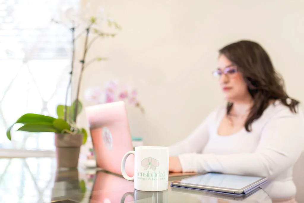 woman working on laptop at a desk with a pink laptop, potted orchid, tablet, and coffee mug