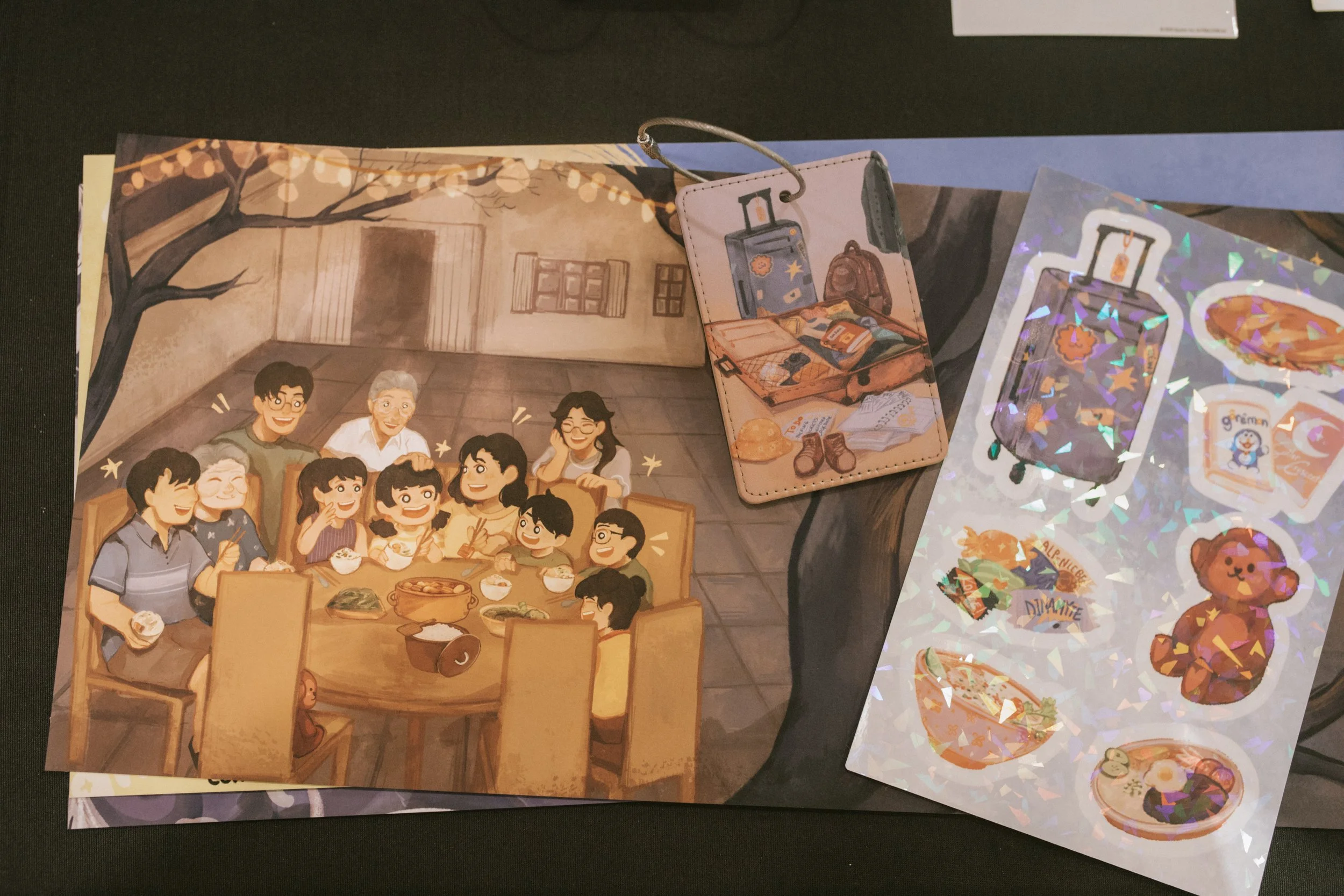 A collection of illustrated paper items, including a family dinner scene, a suitcase with travel items, and holographic stickers.