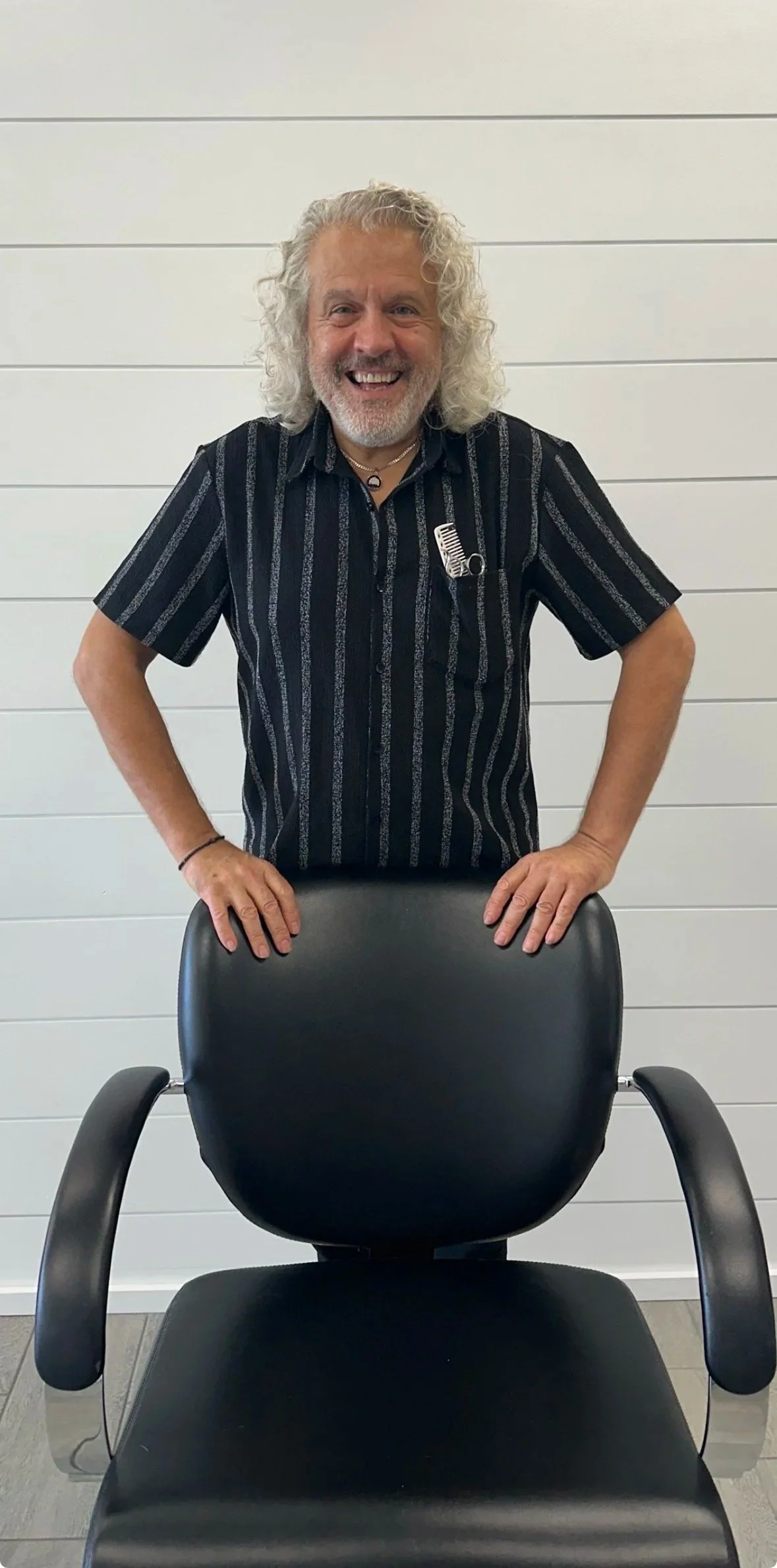 Black and white portrait of an older man with a beard, wearing a dark shirt, smiling with arms crossed.