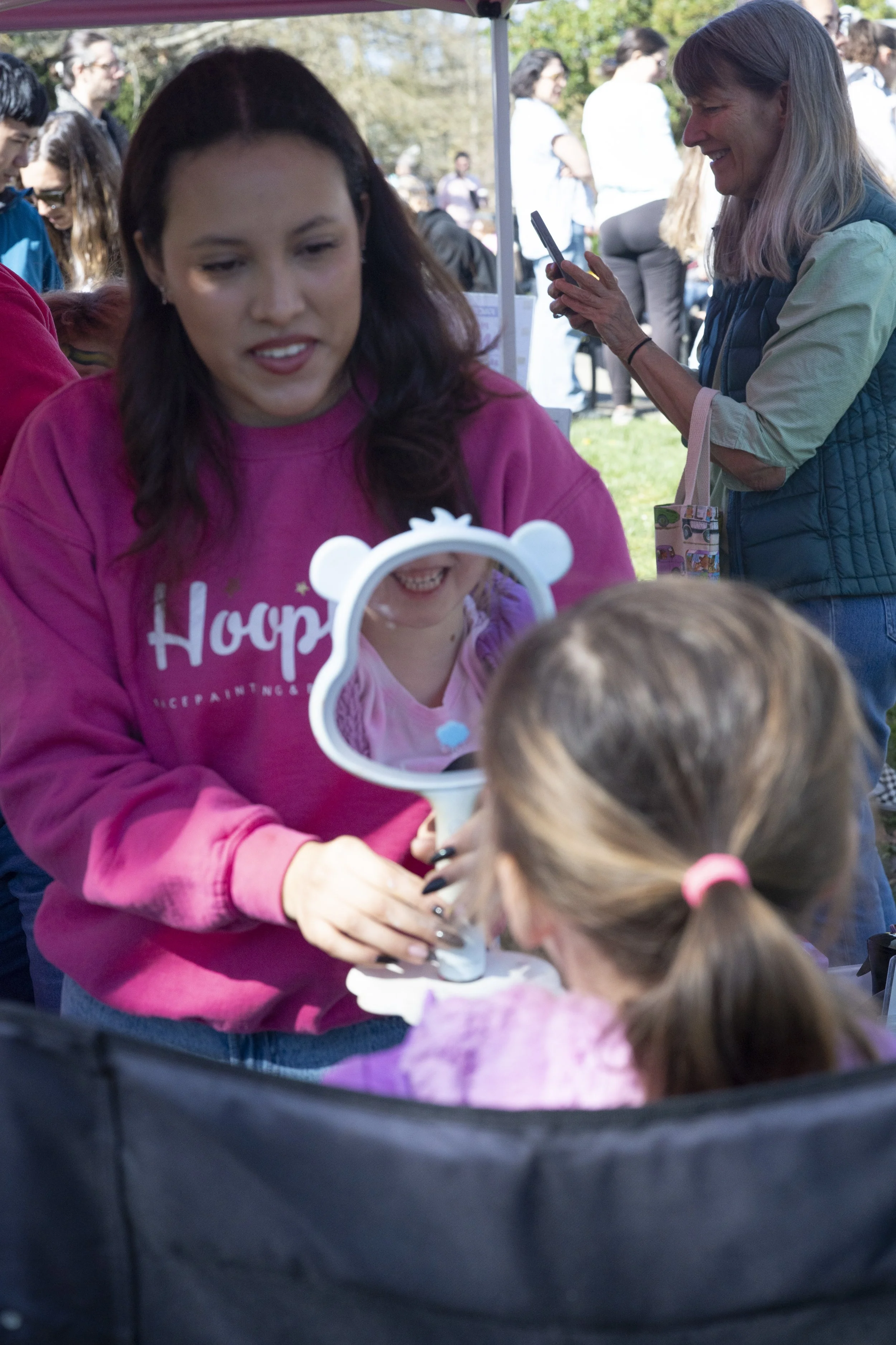 Hoopla face painter holding a mirror up for a little girl