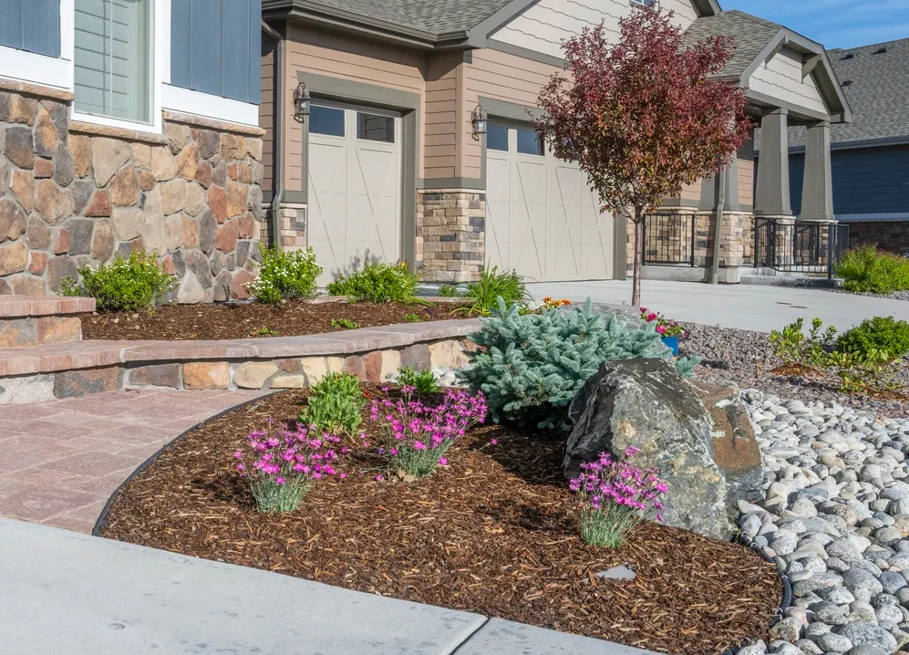 Xeriscape design featuring drought-tolerant plants, natural stone boulders, decorative rock, and mulched garden beds outside a Colorado home.