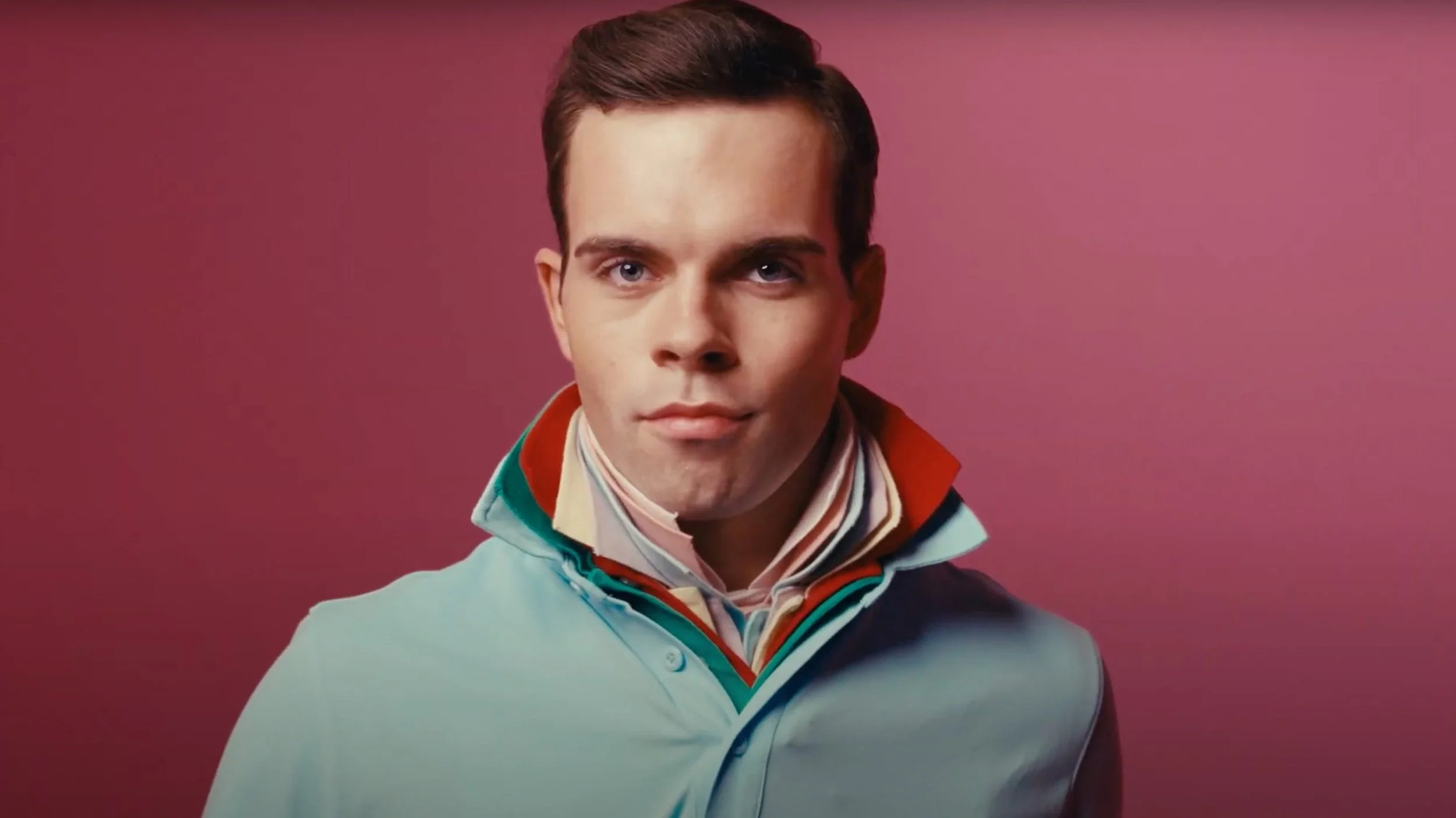 Portrait from Brother Mouth’s Douche Canoe music video, featuring a man against a pink background.