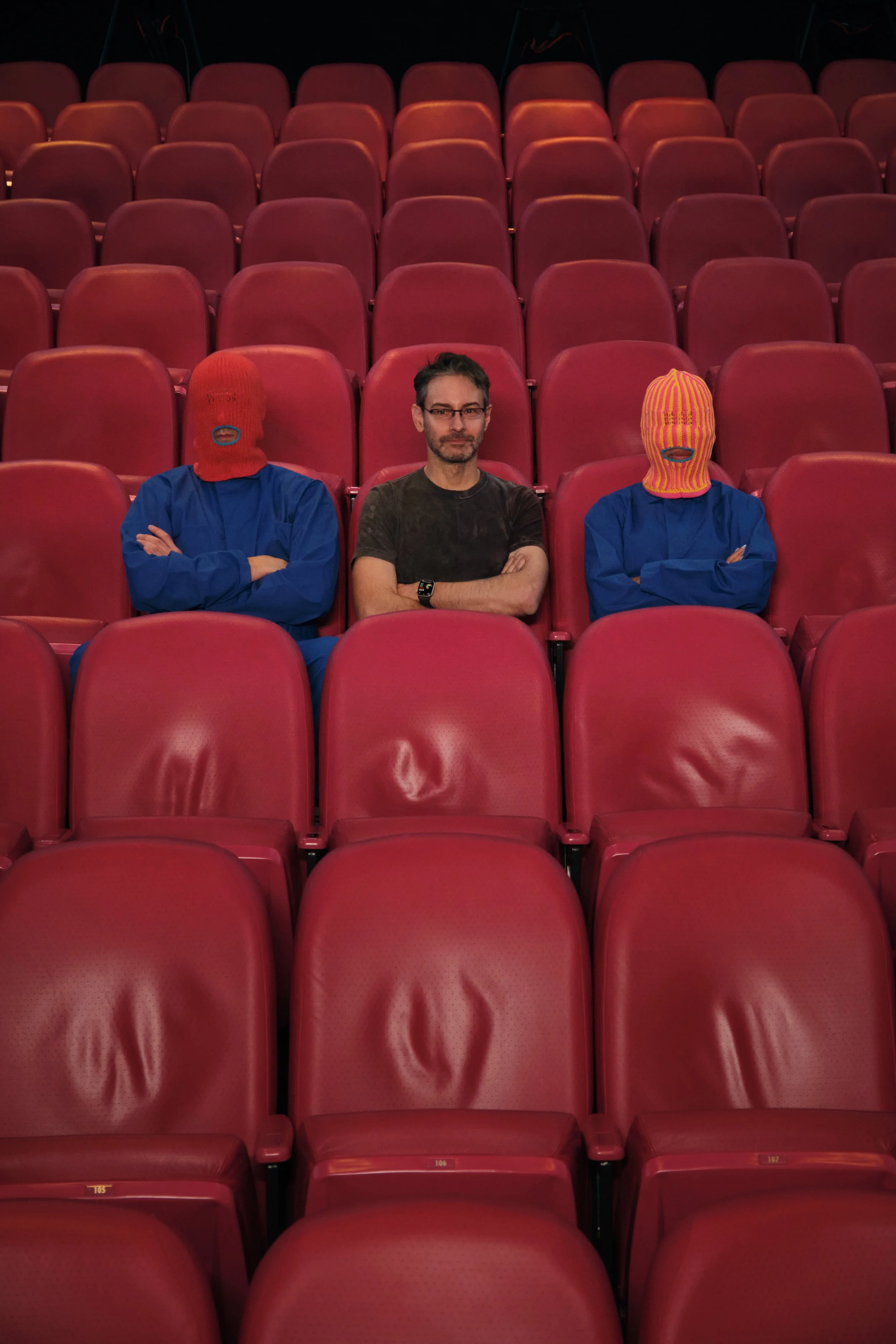 Brother Mouth figures seated in red theater seats with director between them
