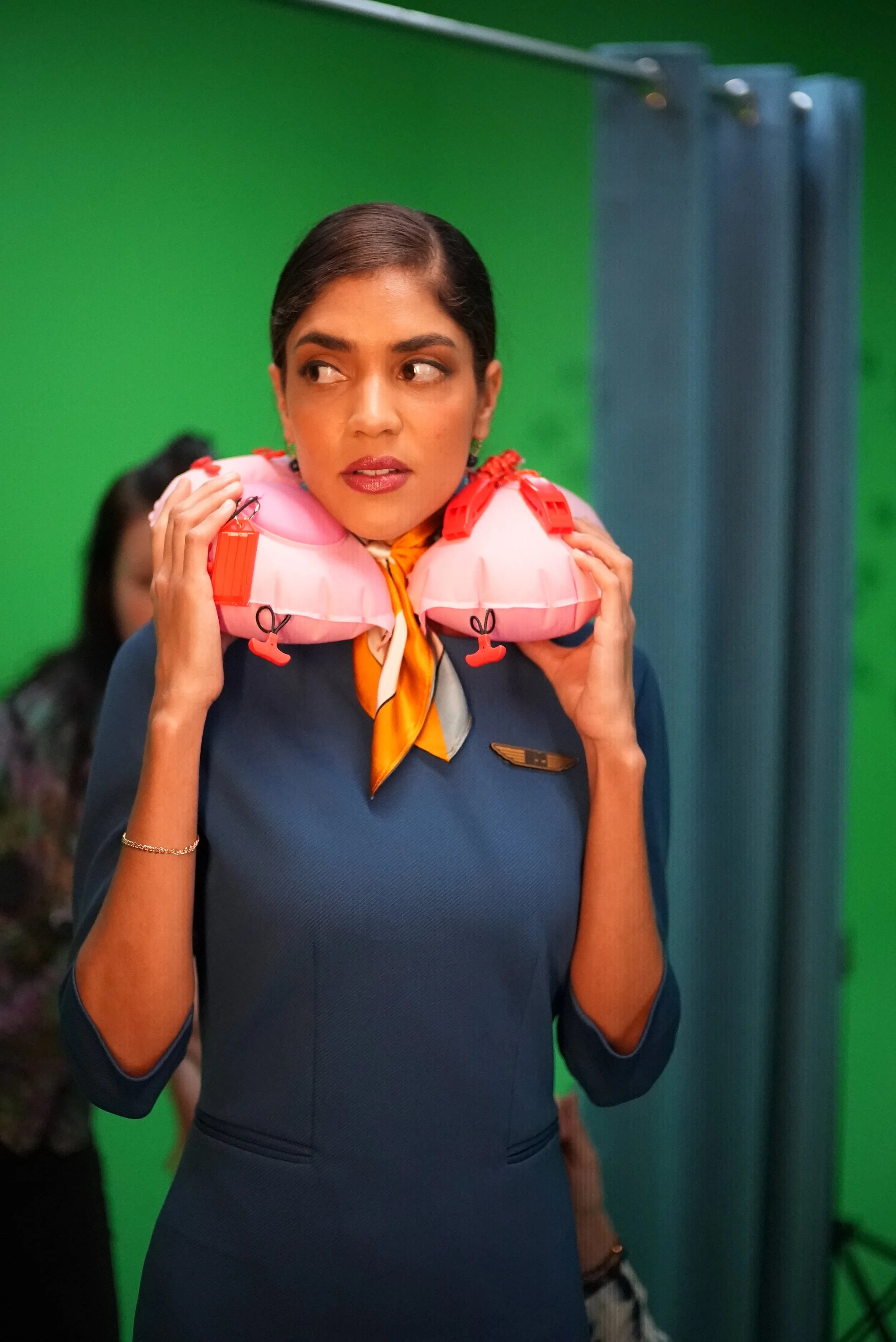 Flight attendant from Brother Mouth’s Neck Pillow project holding a pink neck pillow against a green-screen background.