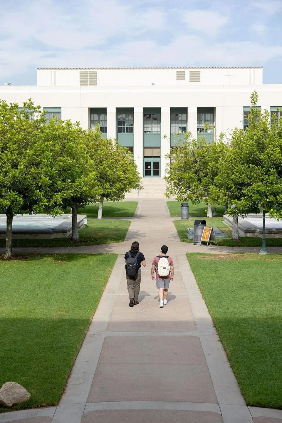 Students walking across a university campus toward an academic building.