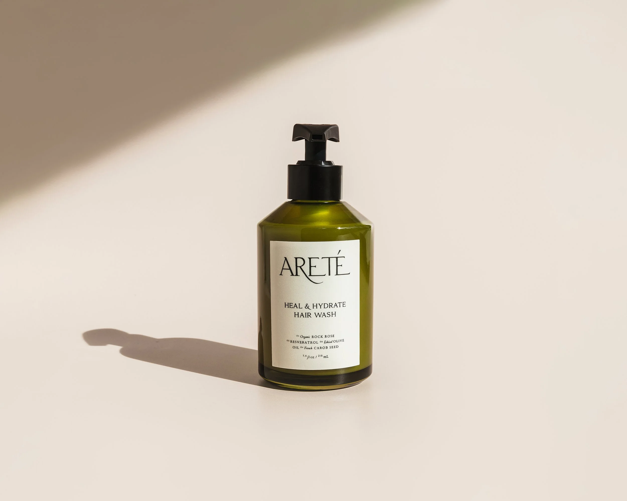 Green bottle of Areté Heal & Hydrate Hair Wash with pump dispenser on a neutral background