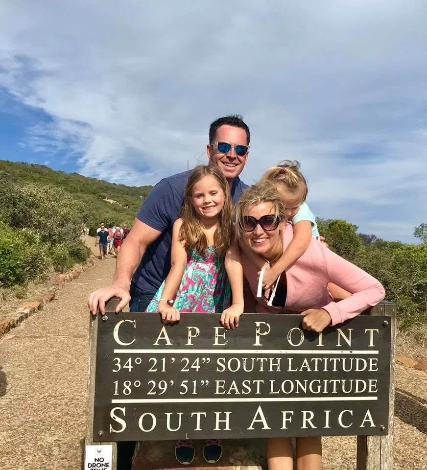 Webb family posing beside the Cape Point sign in South Africa, showing geographic coordinates