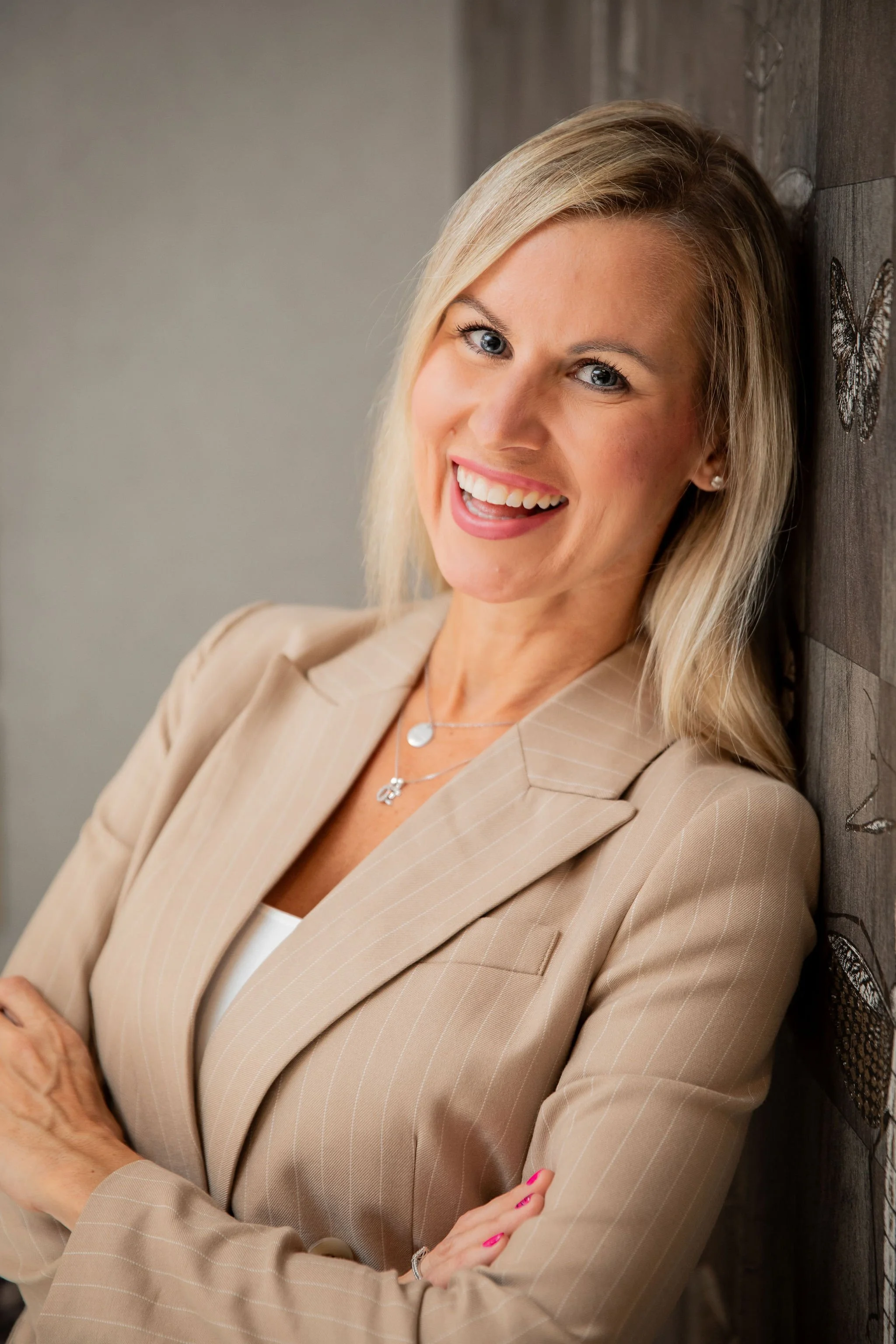 Smiling blonde woman in a beige pinstripe blazer posing indoors