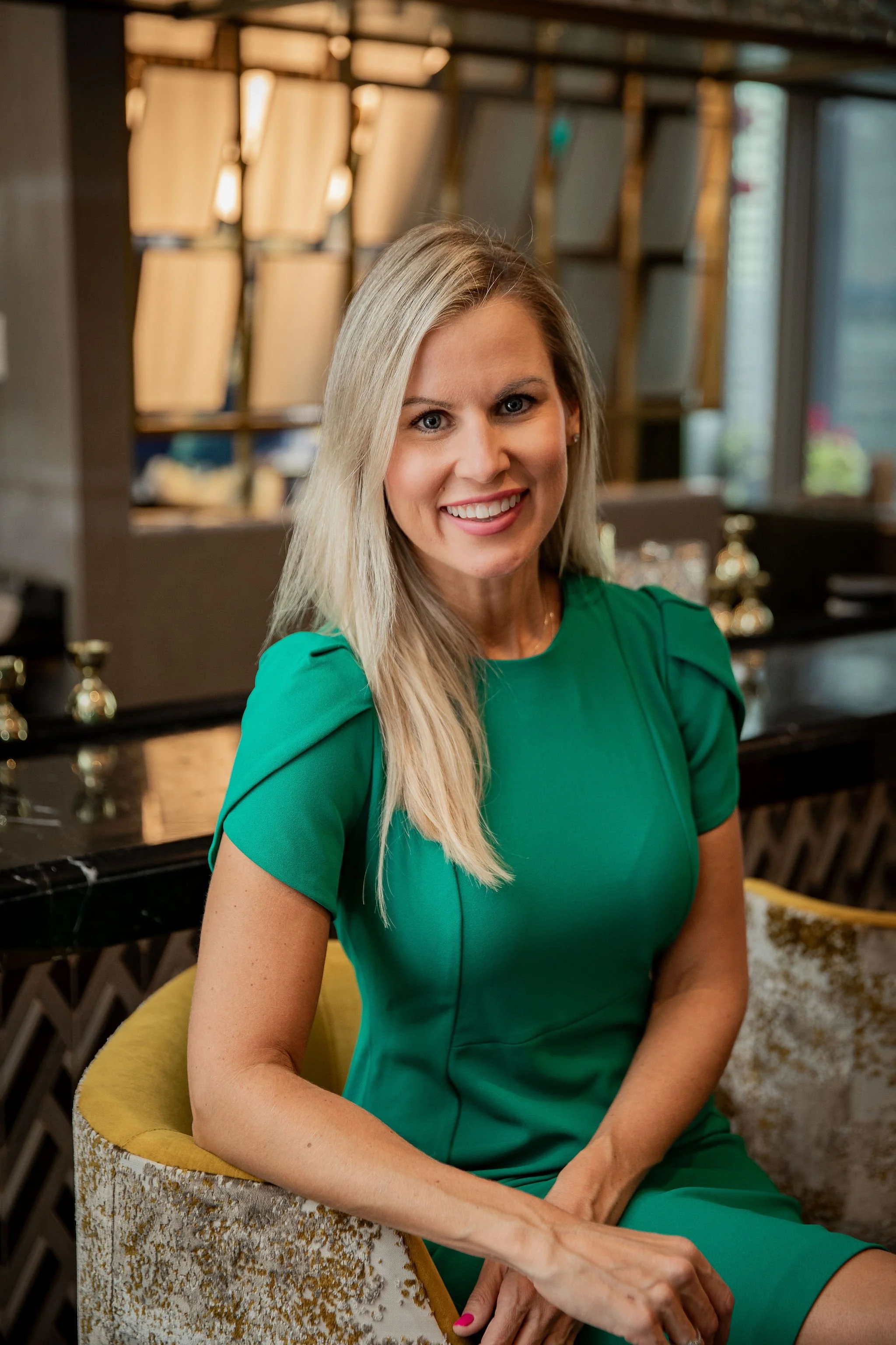 Smiling blonde woman in a green dress seated in a warmly lit room