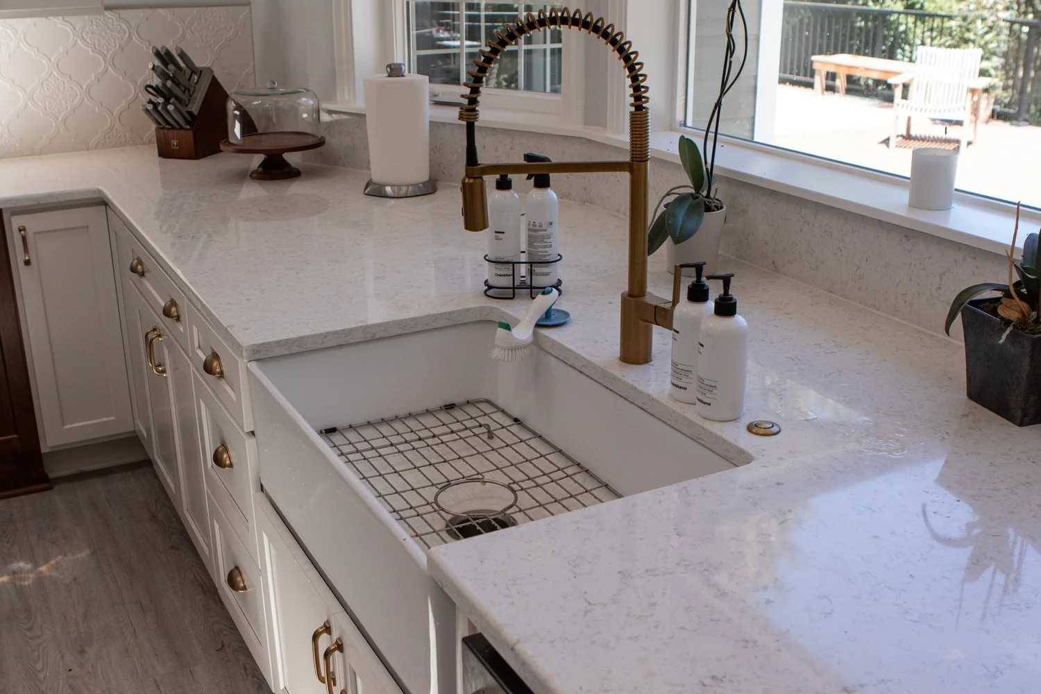 A farmhouse sink with a brass faucet and quartz counter