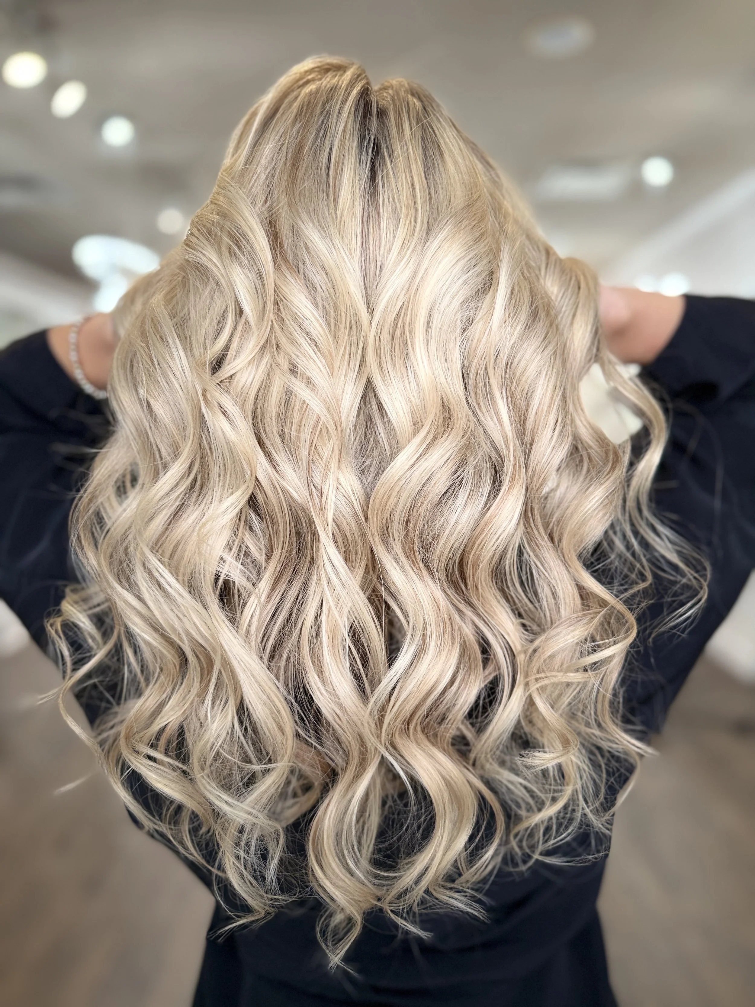 Back view of long, wavy hair featuring full blonde highlights blended with a natural brunette base — showcasing dimensional color and shine at Pani Style Hair Salon in Katy, TX.