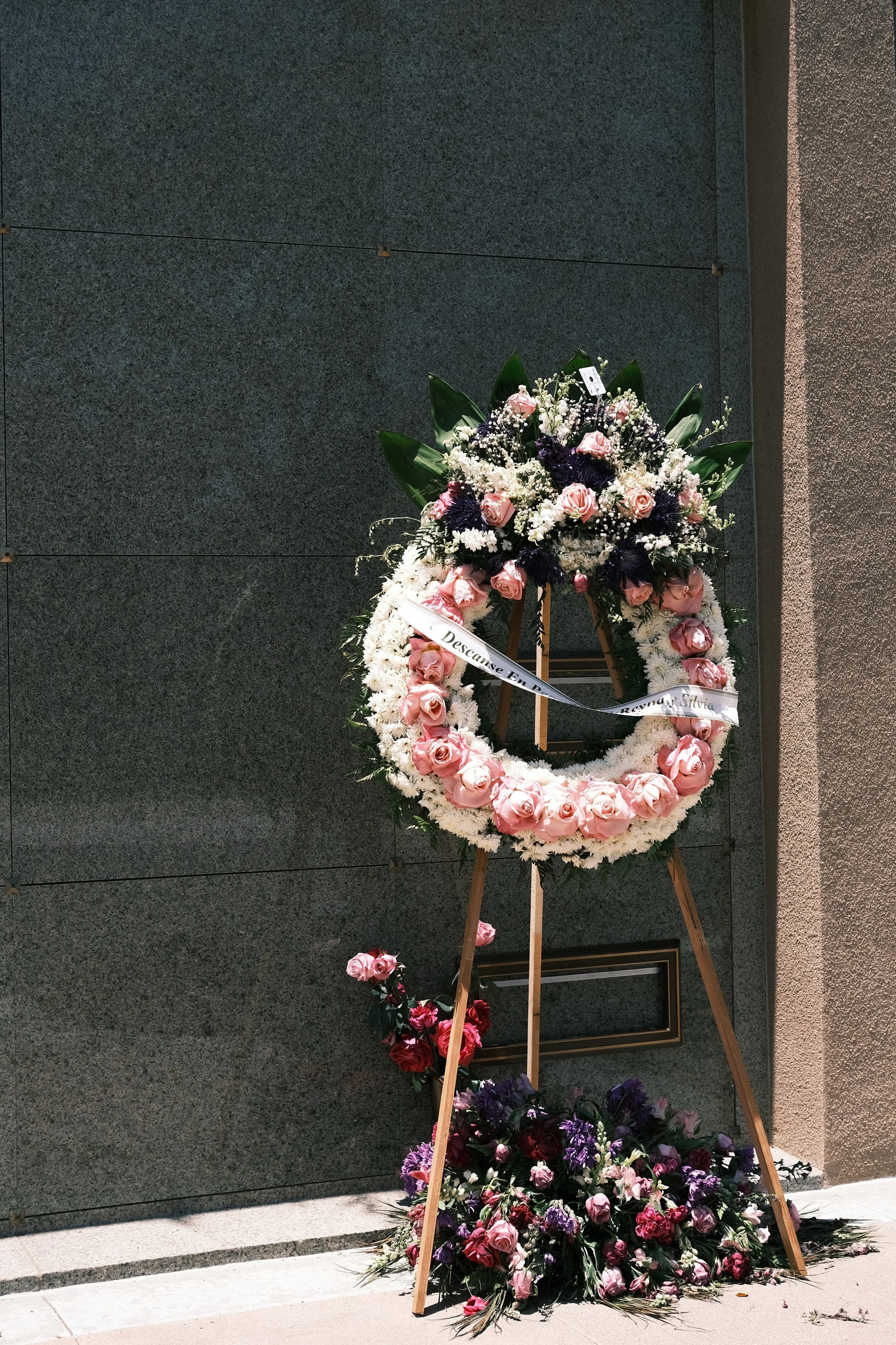 A round flower wreath with pink and white flowers against a mausoleum wall crypt