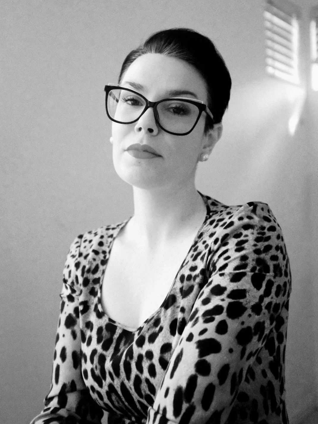 Black and white portrait photograph of Sara Matzenbacher, a female end of life photographer and funeral director and advisor wearing a dolce and gabanna leopard top and black cat eye glasses