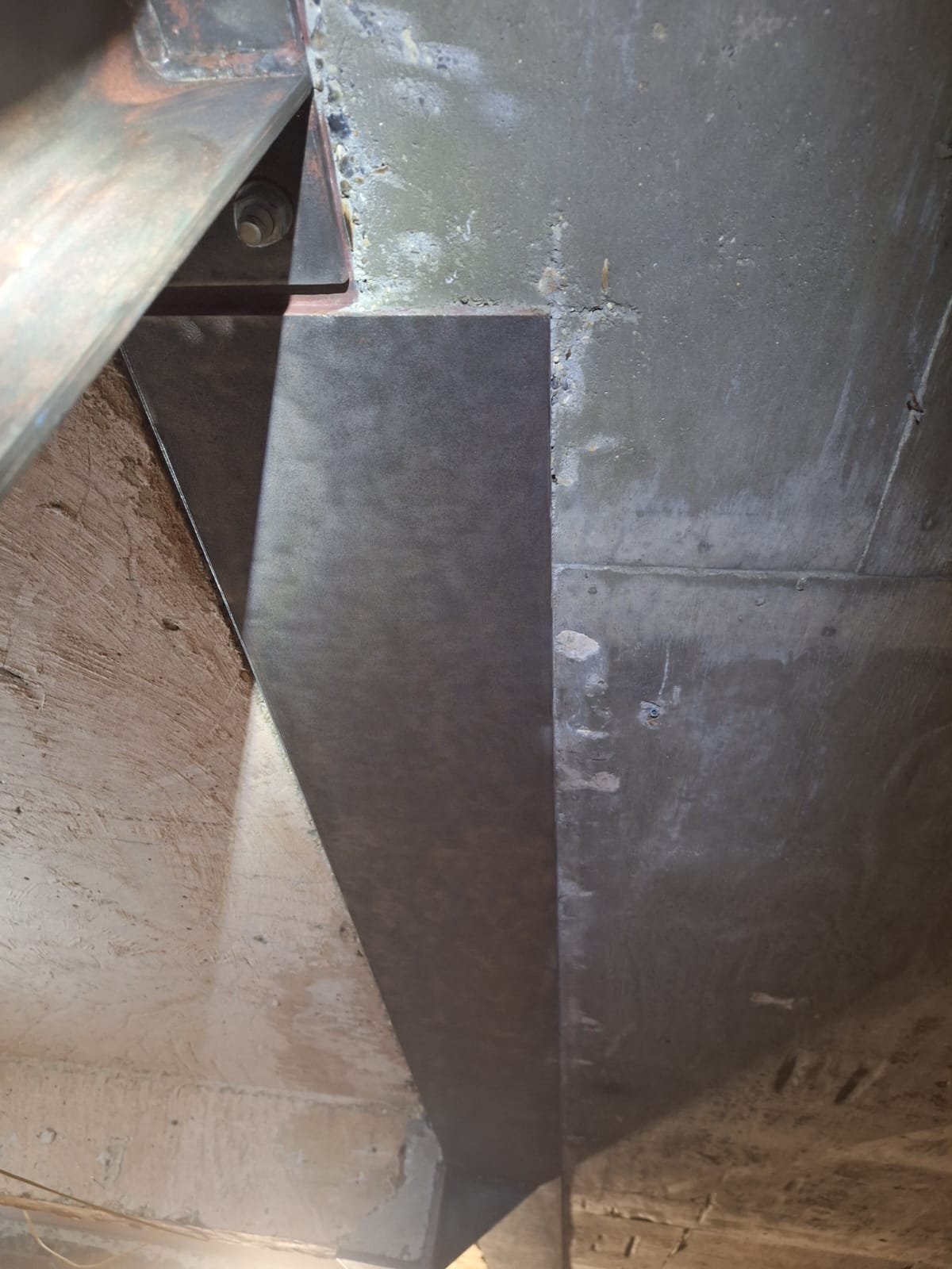 Close-up of a metal support beam attached to a concrete wall and a wooden surface.
