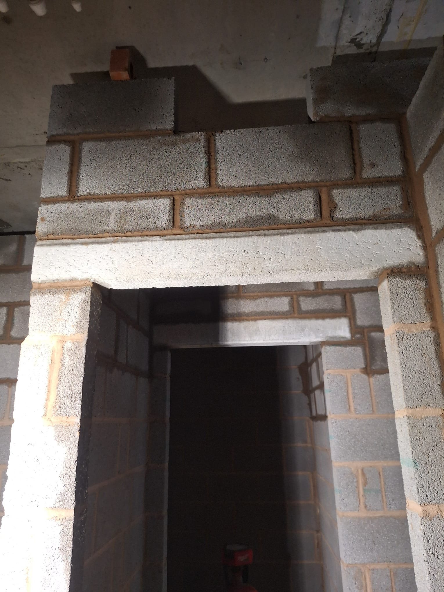 A construction site with unfinished brick walls and concrete beams in a dimly lit space.