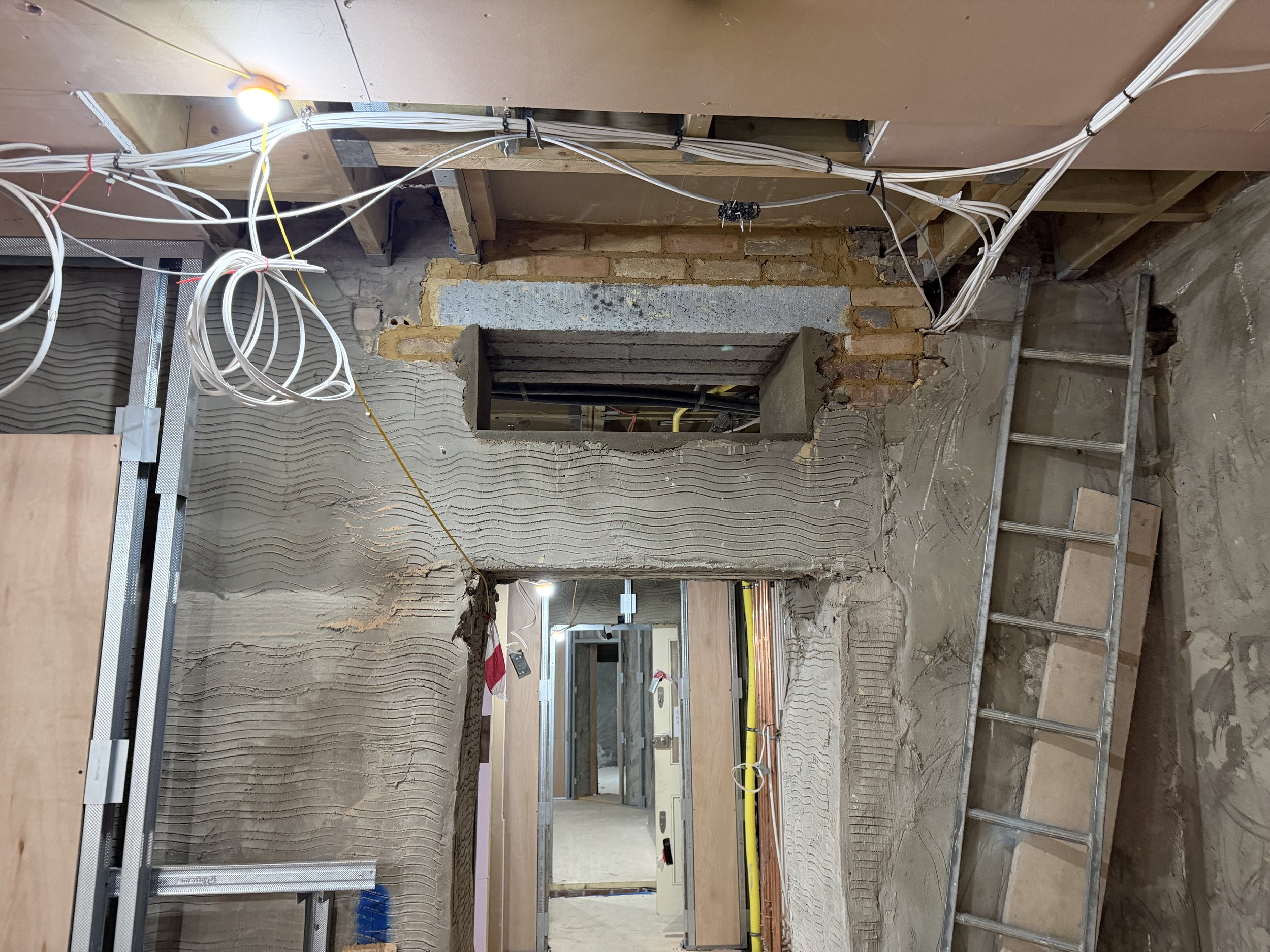 Construction site with exposed electrical wiring, drywall, and bricks, with construction tools and materials visible.