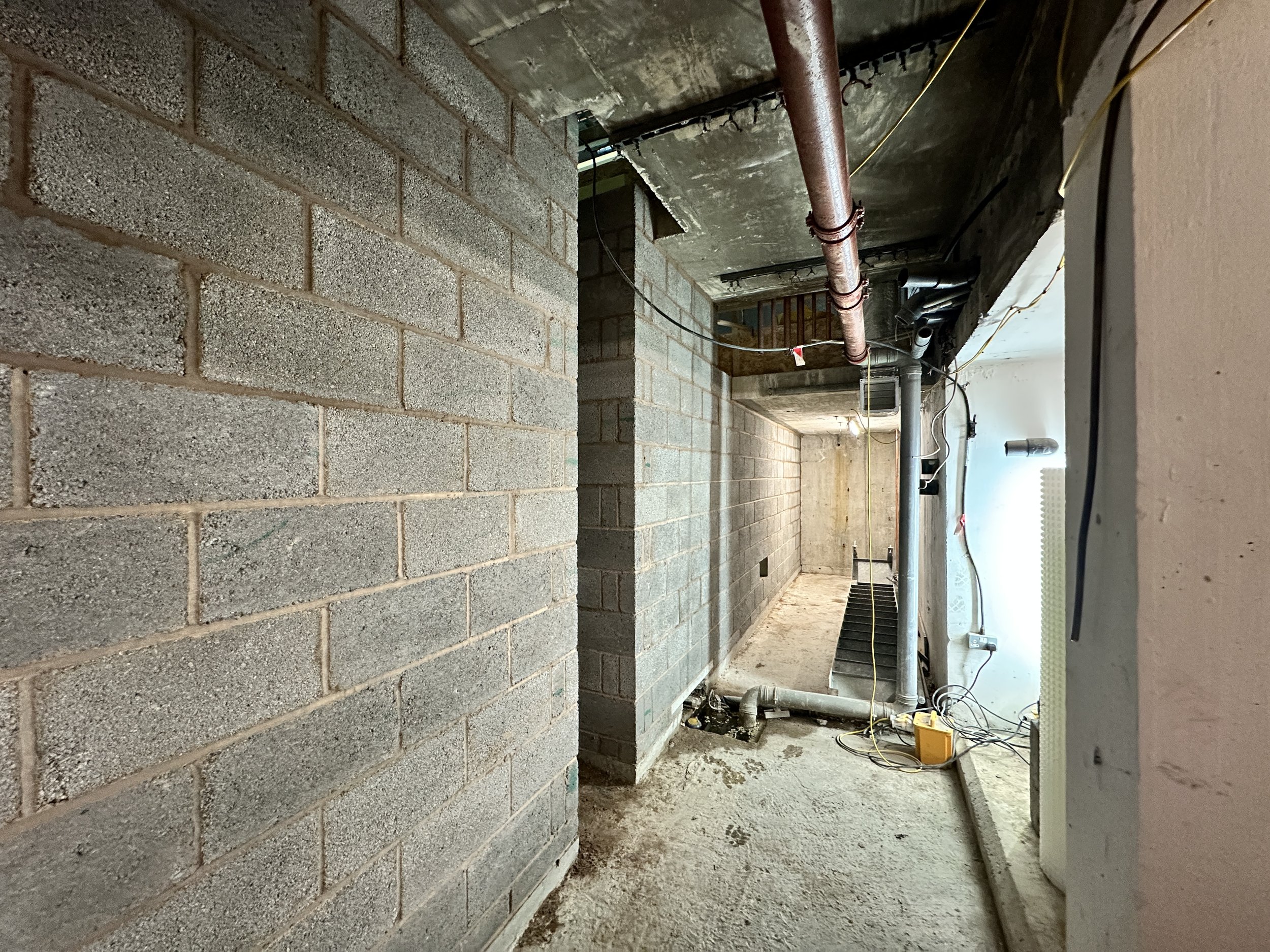 Construction site with unfinished brick walls, plumbing pipes, and electrical wiring in a building under construction.
