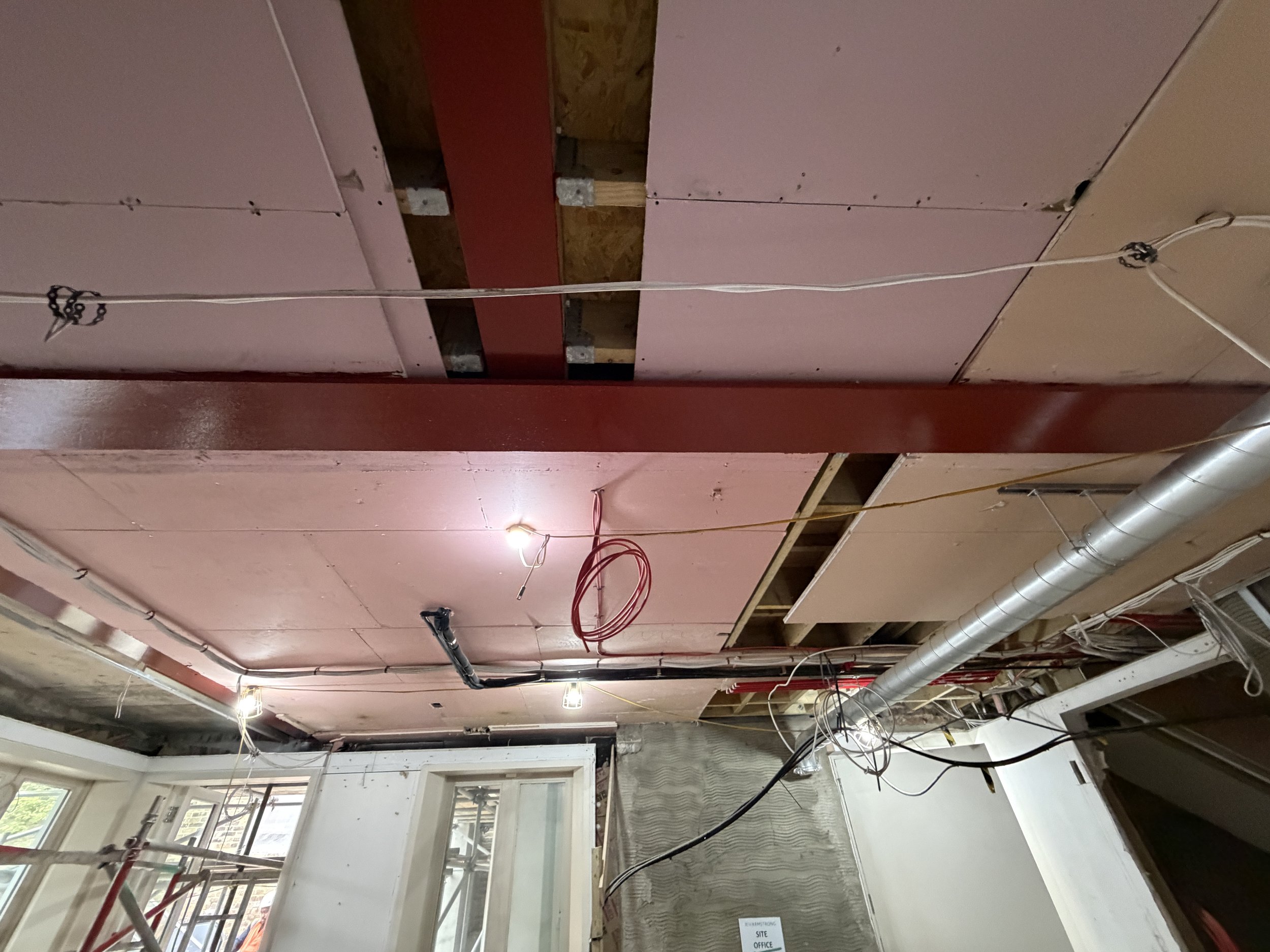 Interior of a building under construction with exposed ceiling, electrical wiring, and ductwork.