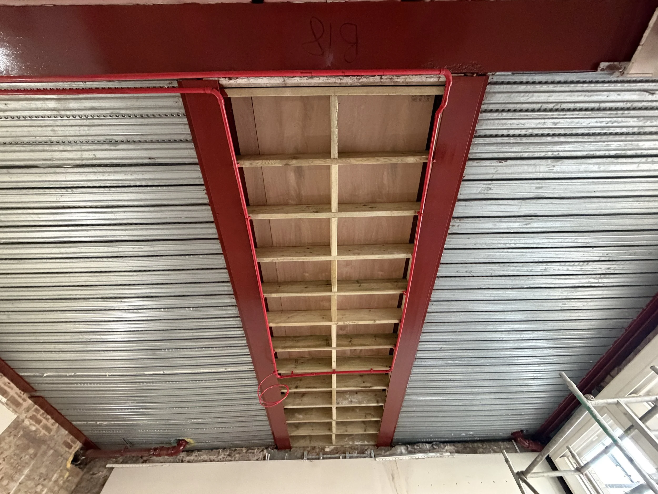 Construction ceiling showing exposed wooden framing and red metal structural support with electrical conduit.