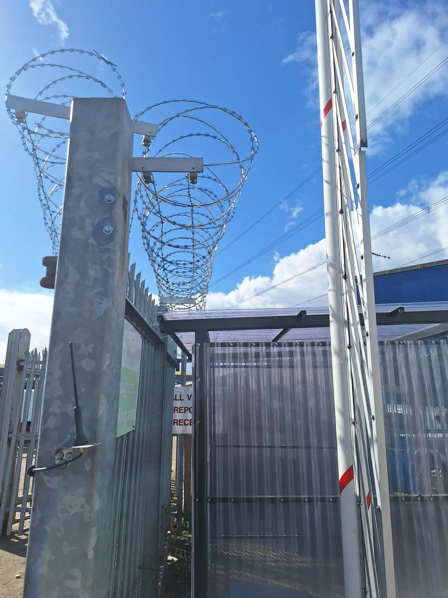 Security gate with barbed wire and a sliding barrier on a sunny day with a blue sky.