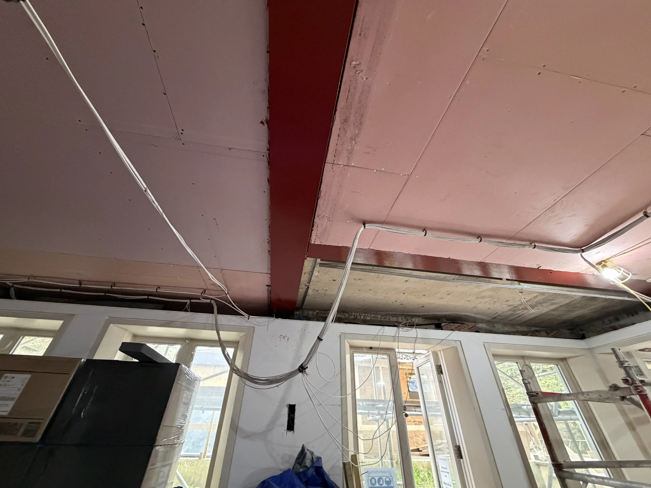 Interior of a room under construction with unfinished walls, visible wiring, and windows letting in natural light.