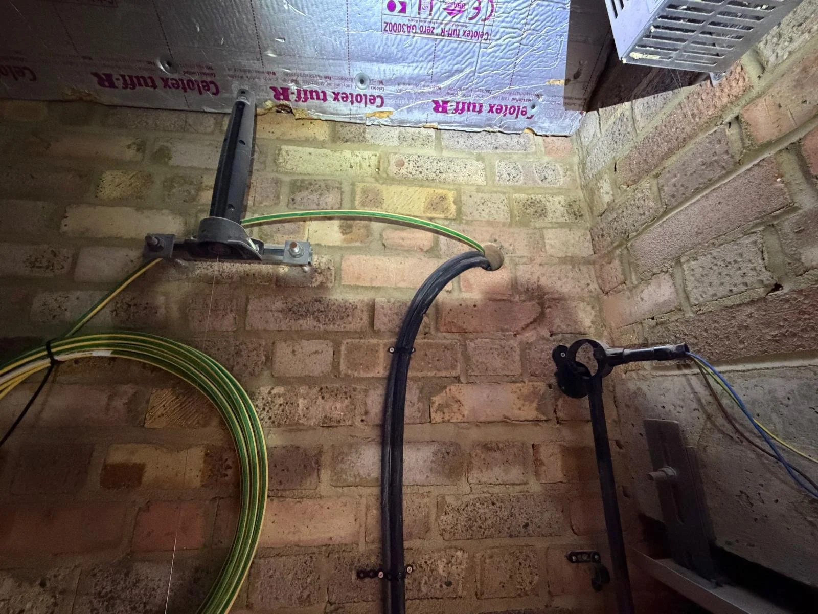 View of an unfinished brick wall with electrical wiring, conduit, and mounted hardware for electrical or network installation.