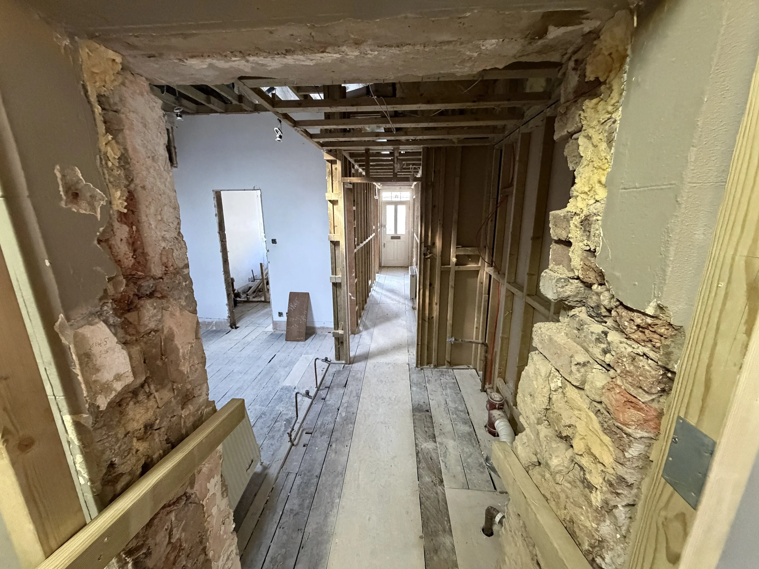 Room under construction with exposed wooden framing, insulation, and partially demolished wall framing.