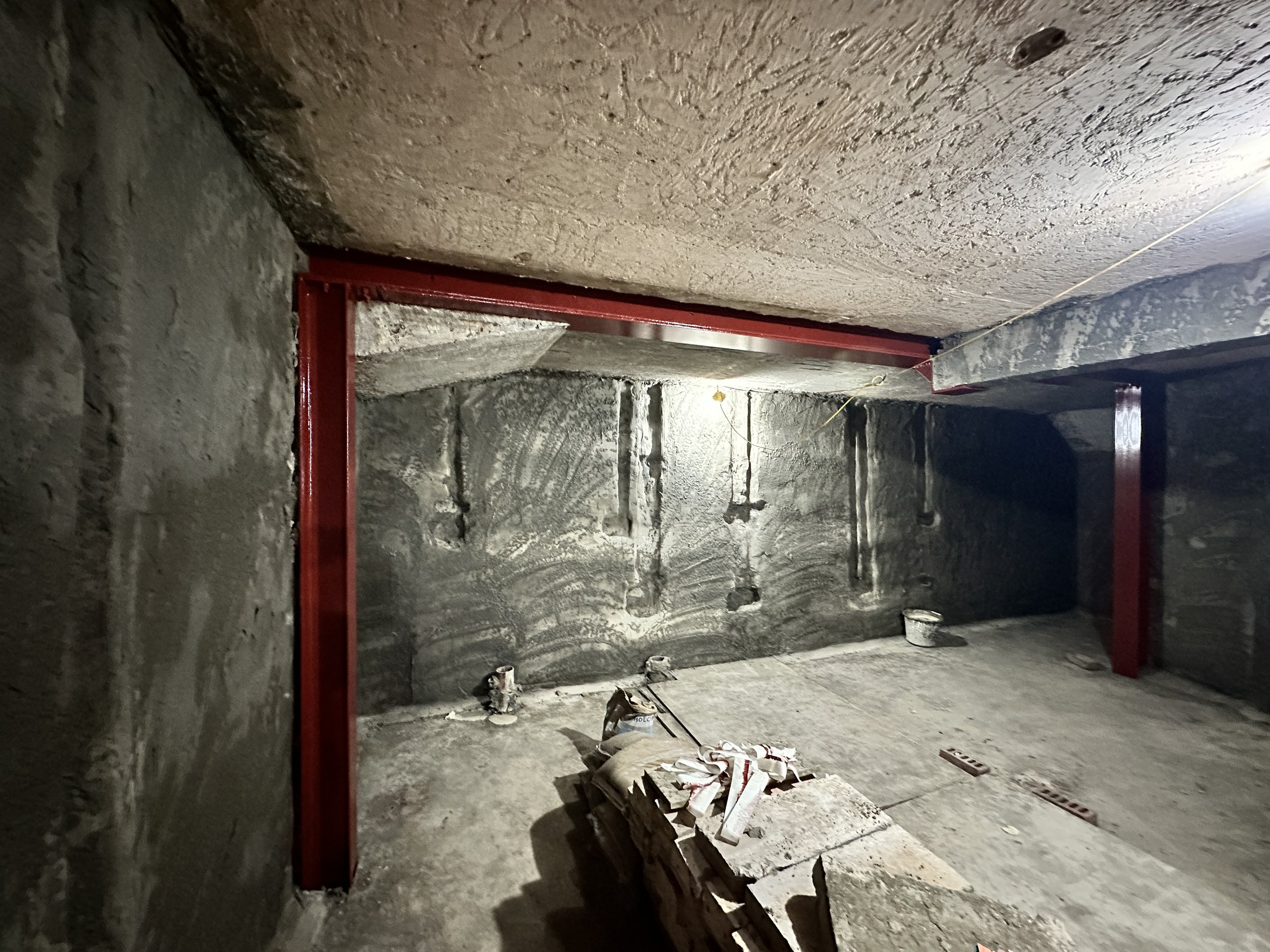 Construction site with concrete walls, red steel beams, and building materials on the floor.