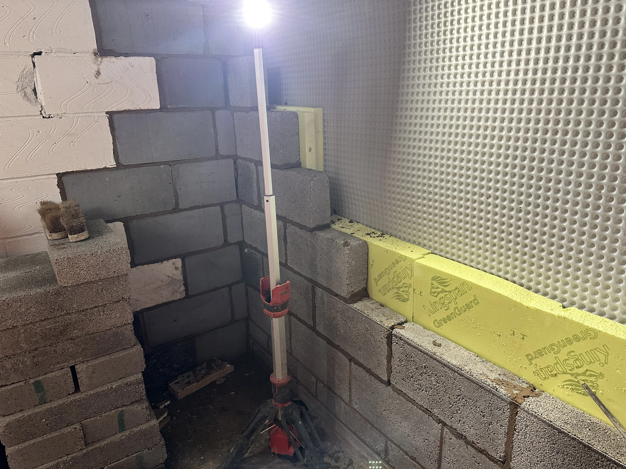 Construction site with stacked bricks, a level, and yellow insulation foam on the right wall.