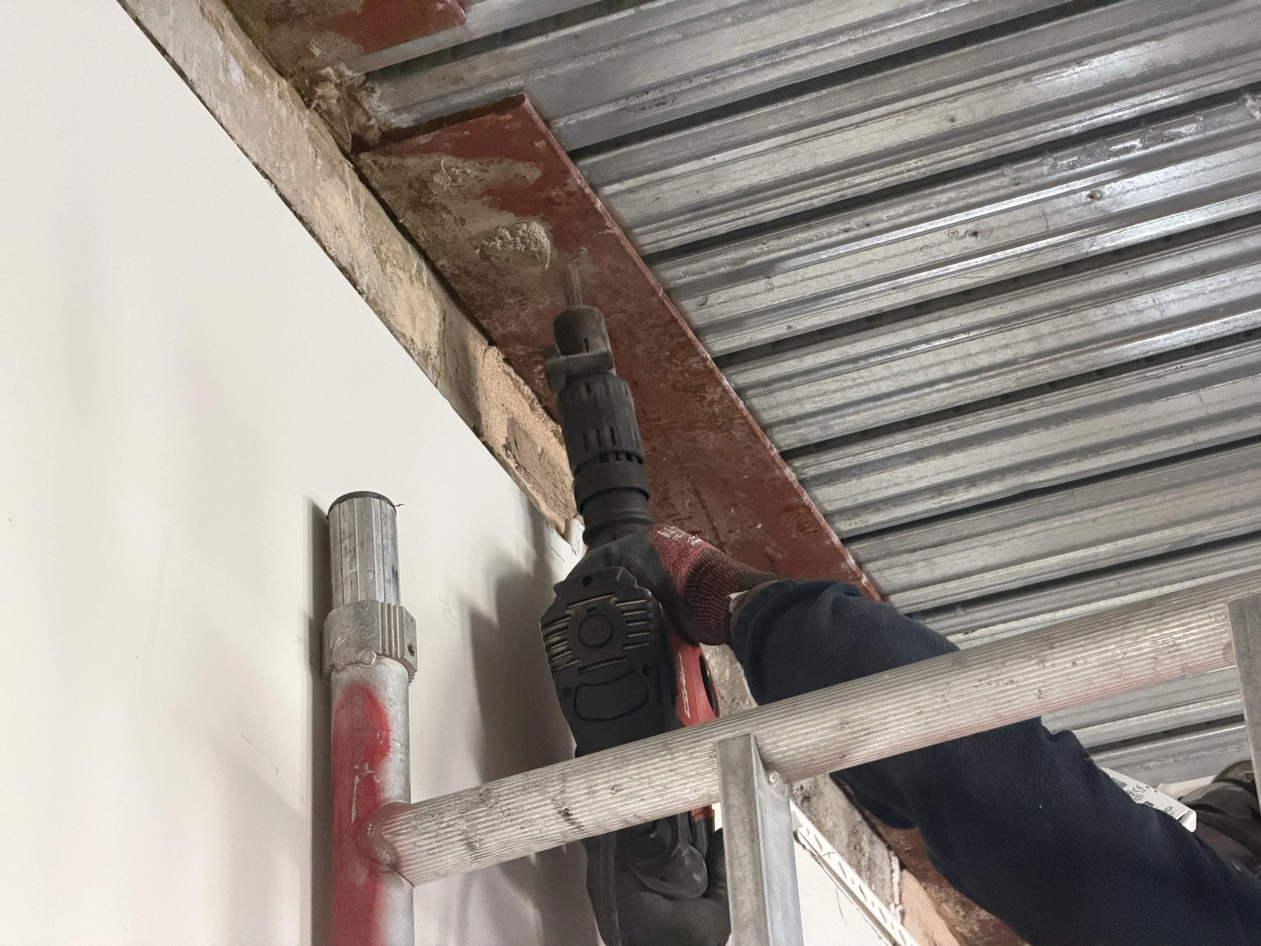 Person using a power drill on a metal and brick wall during construction or renovation work.
