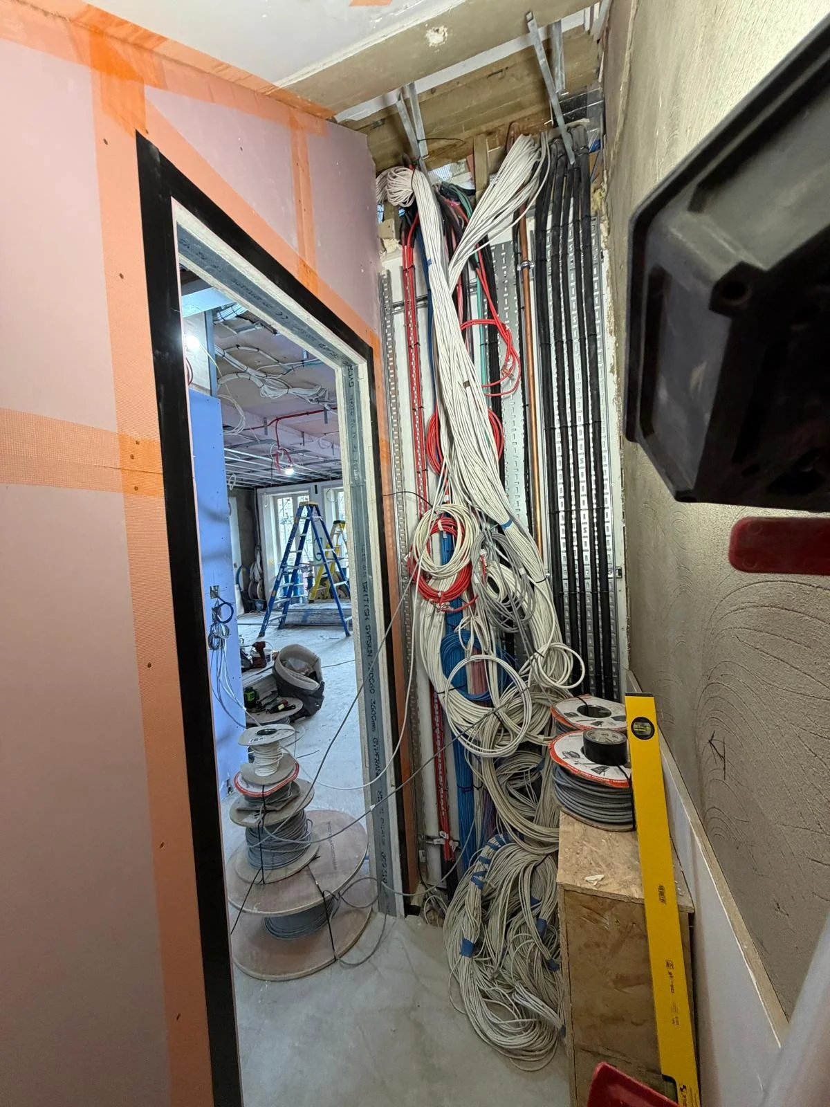 View of an electrical wiring and construction site inside a building with cables, tools, and unfinished walls.