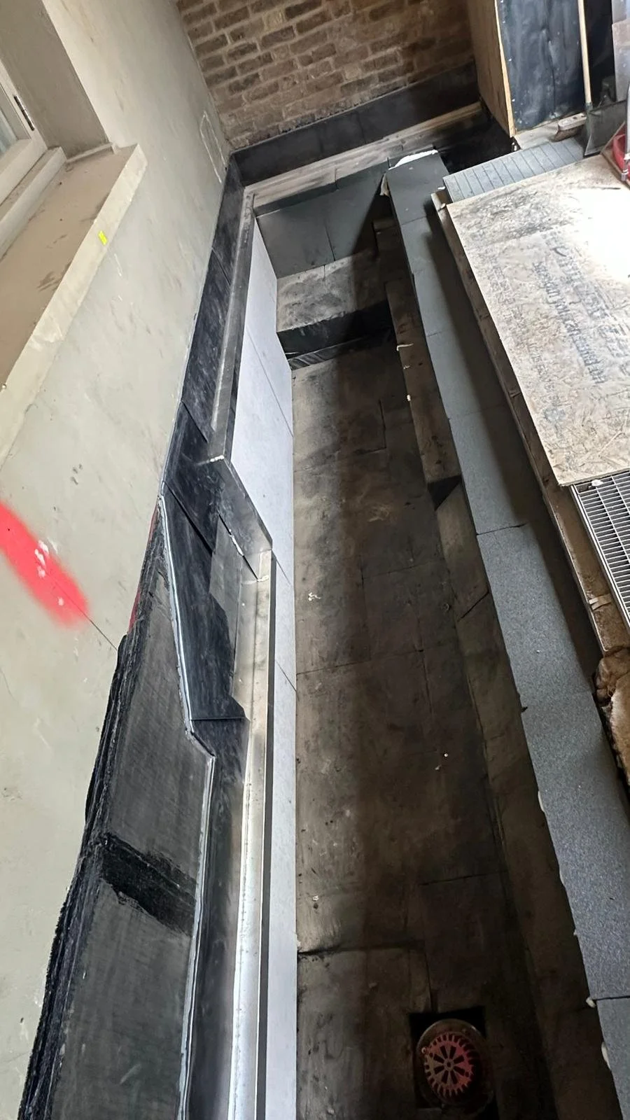 Construction site with black stone or metal countertops, partially installed, and unfinished surfaces, showing a sink cutout and plumbing drain.
