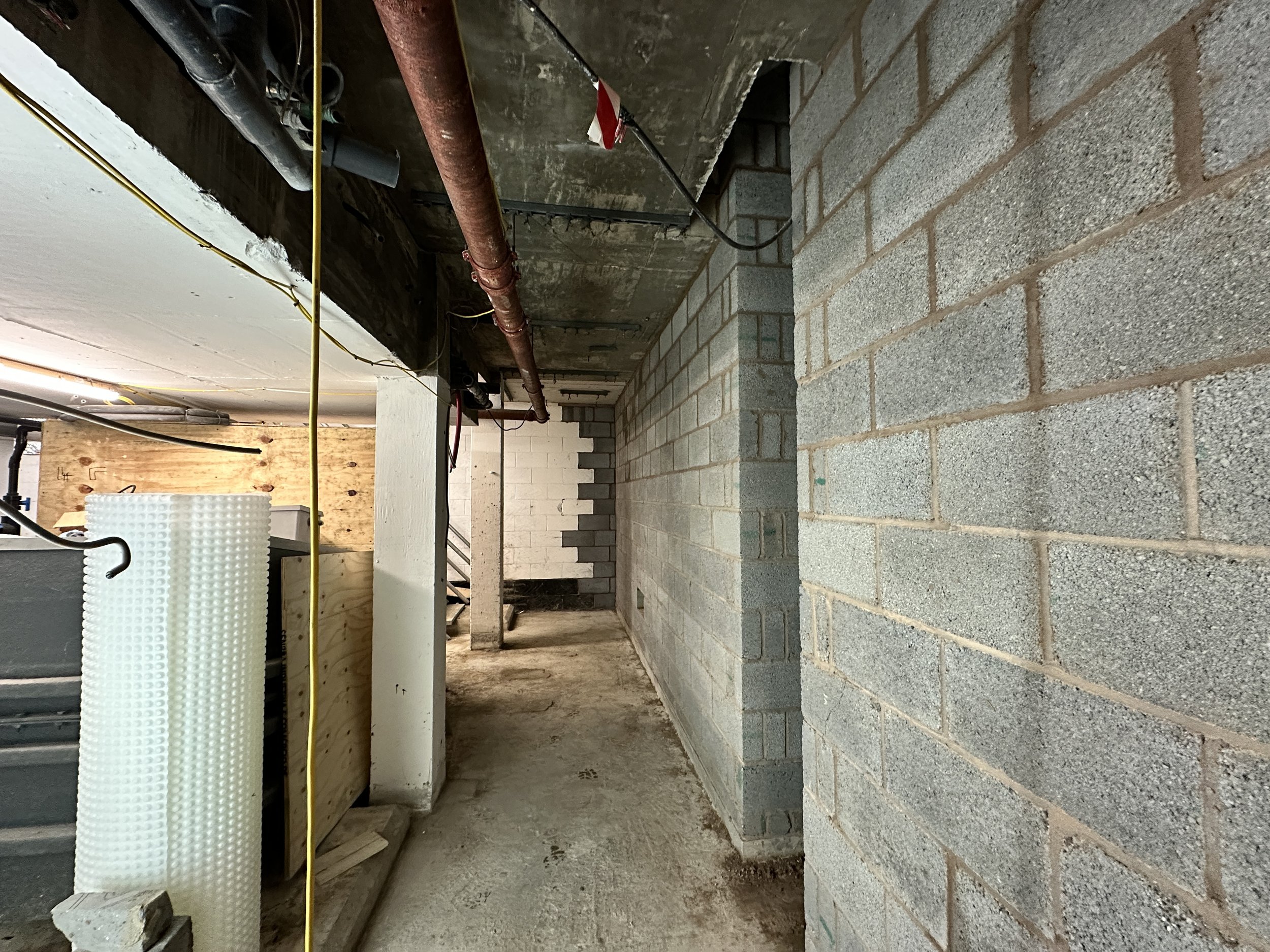 Construction site with cinder blocks and cinder block wall, pipes, and electrical wires.