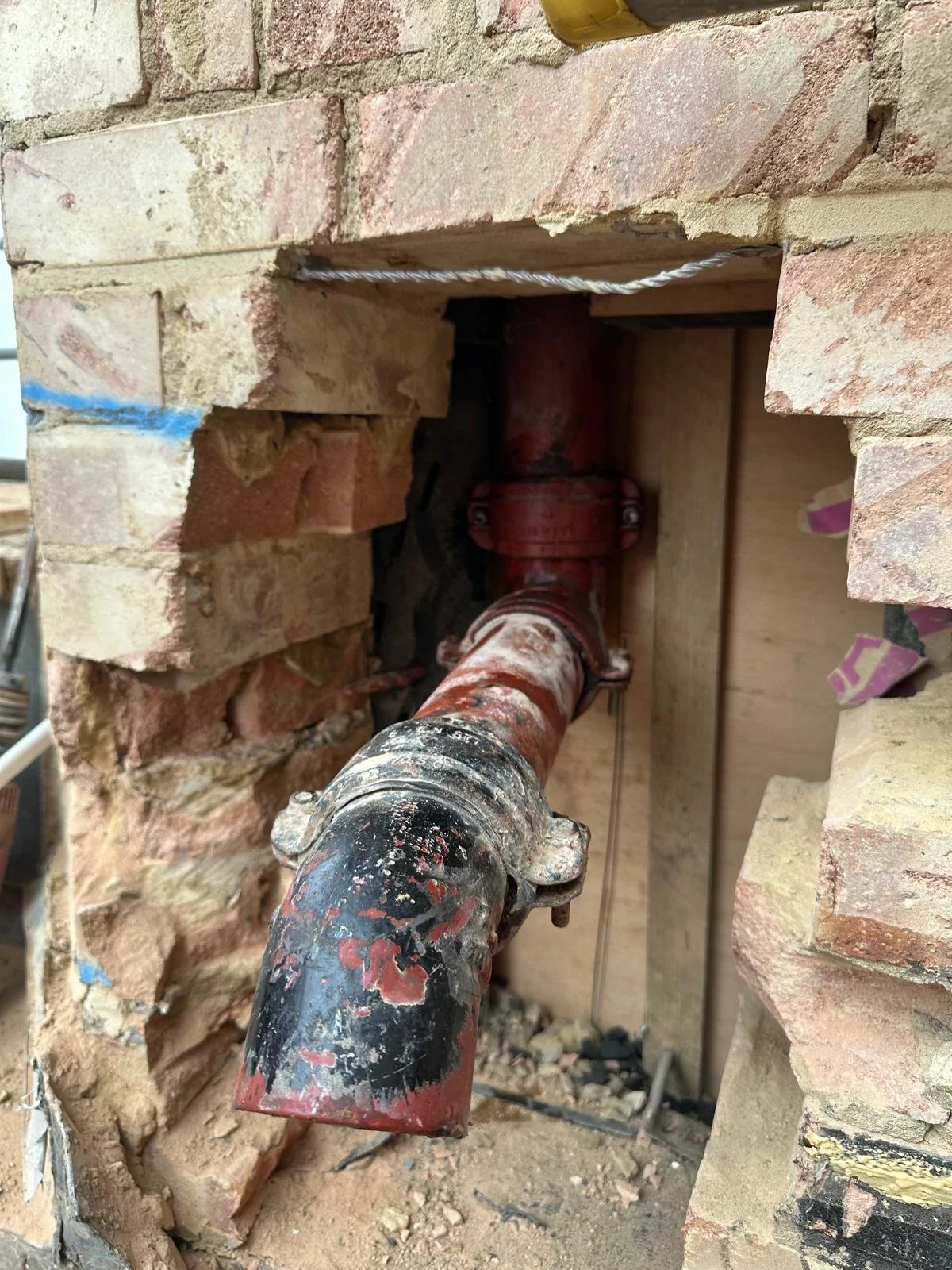 A close-up image of a red pipe in a drywall opening, part of a plumbing installation within a brick wall.