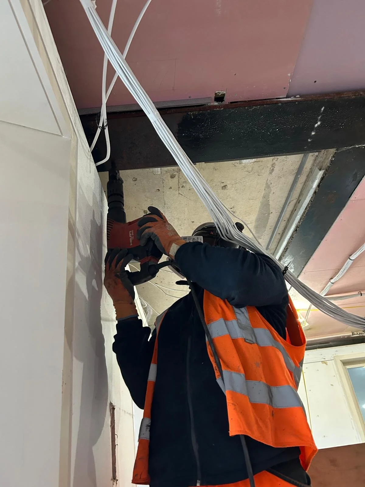 Worker in safety vest and gloves installing electrical cables in a construction site.