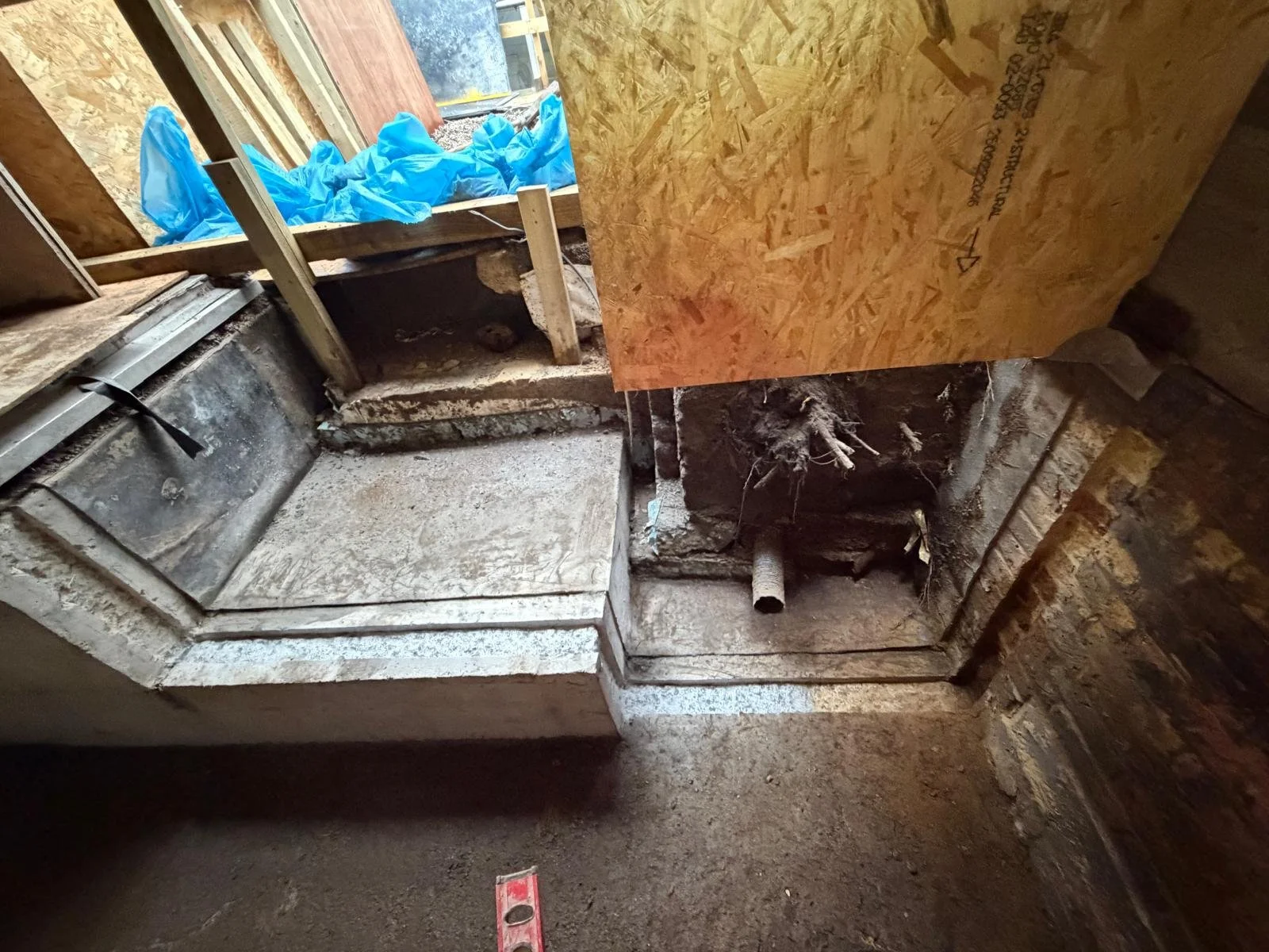 View of a construction site showing an unfinished wall with exposed wooden and brick materials, pipes, and electrical wiring.