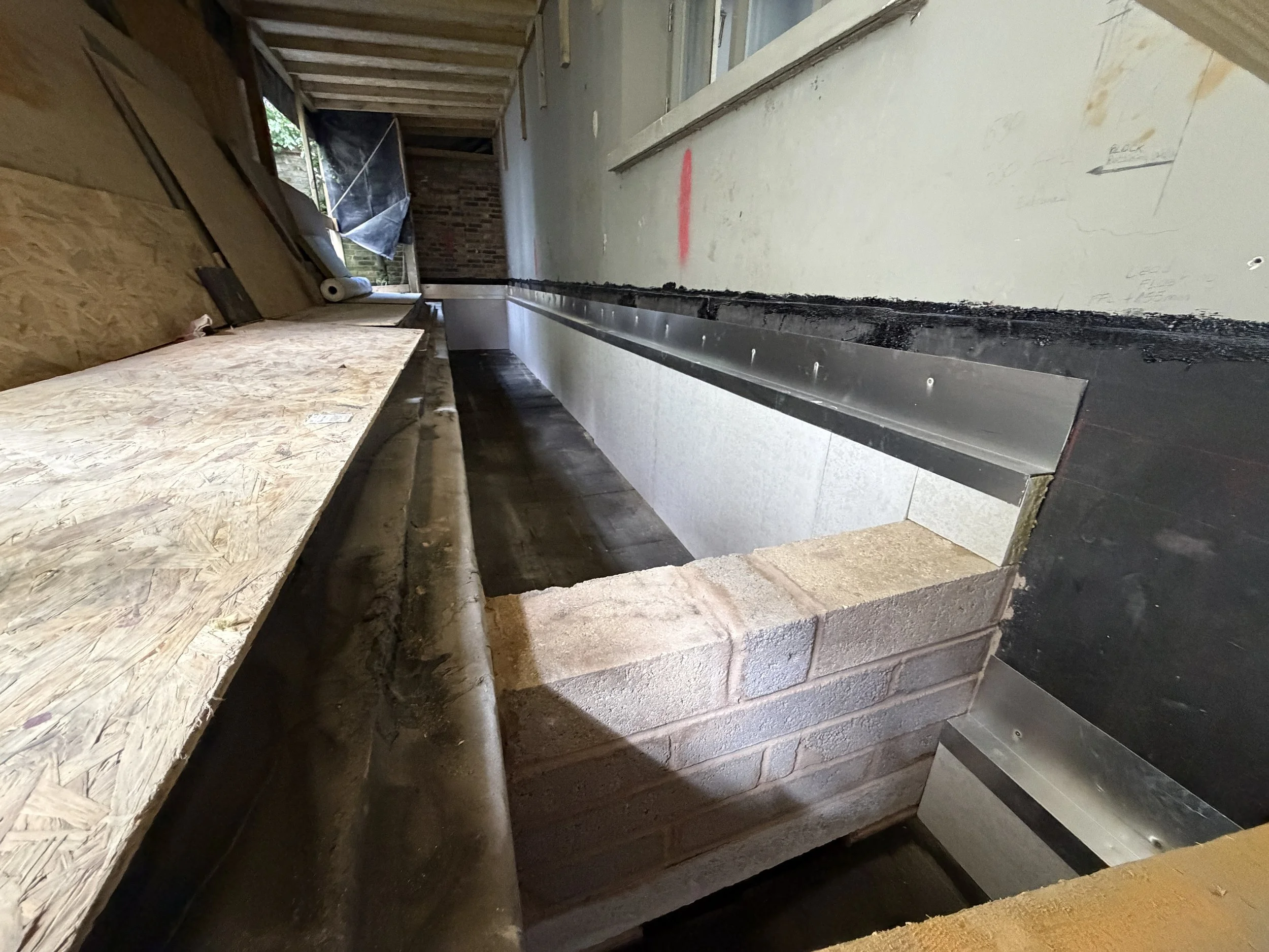 Construction site with partially built concrete and brick walls, wooden framing, and construction materials scattered around.