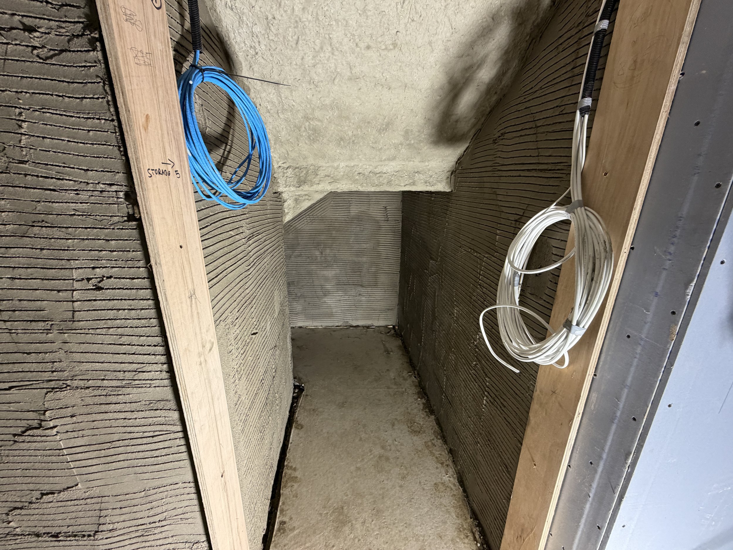 Construction site with electrical wiring coiled on a wooden surface, with a partially built wall and insulation in the background.