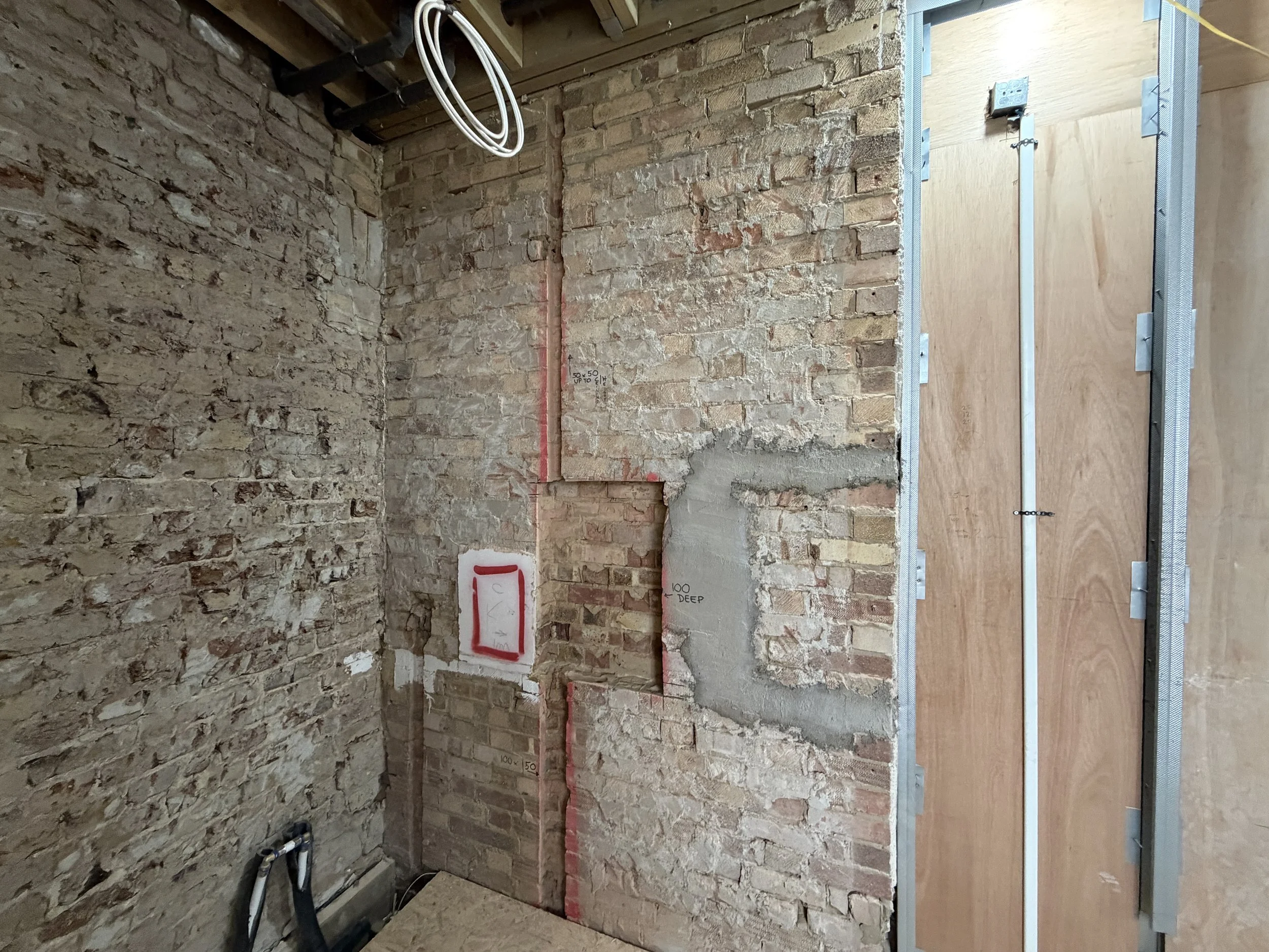 Interior of a building under construction or renovation with exposed brick walls, electrical wiring, and metal framing for drywall installation.