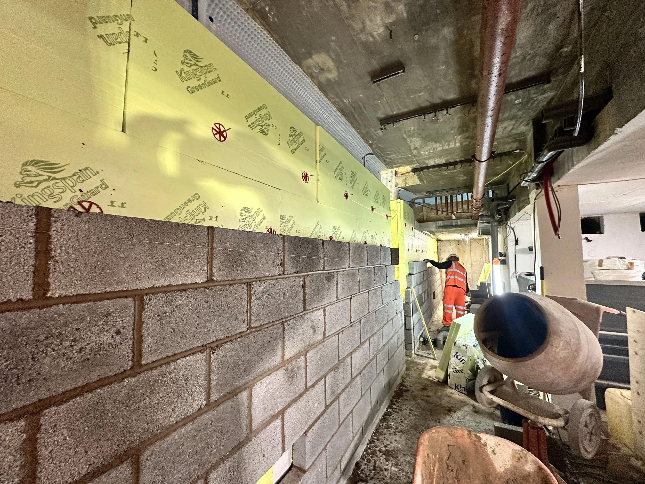 Laying bricks for a wall in an indoor construction site with workers and construction materials visible.
