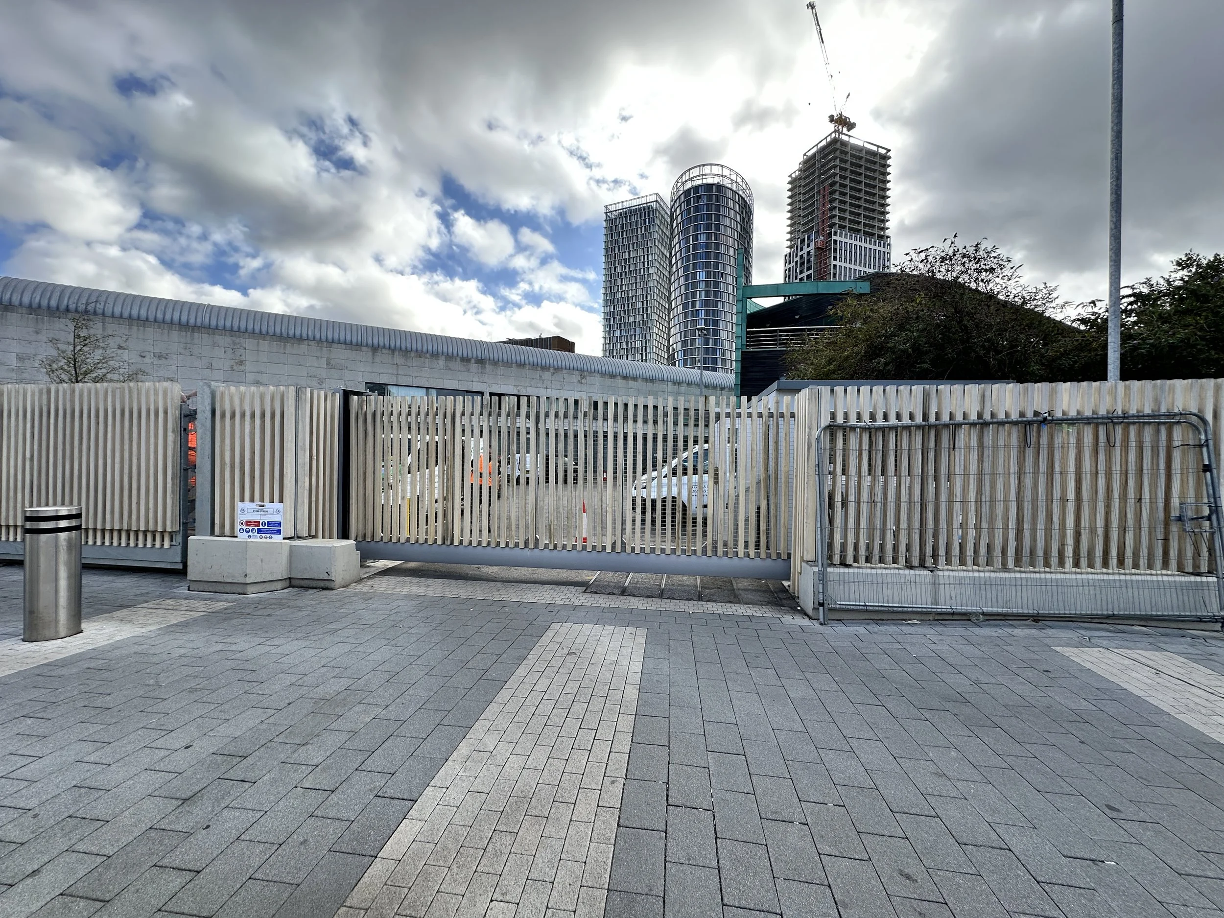 Cityscape with three skyscrapers under cloudy sky, view from a fenced area with gray paving stones.