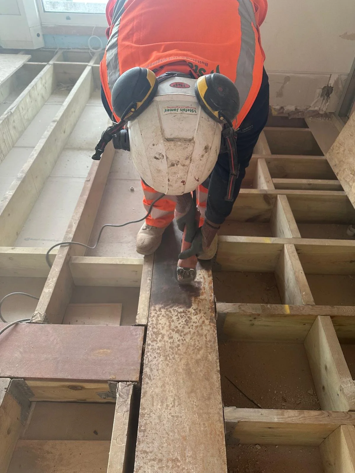 Construction worker cutting a metal piece with an electric saw on a wooden framework.