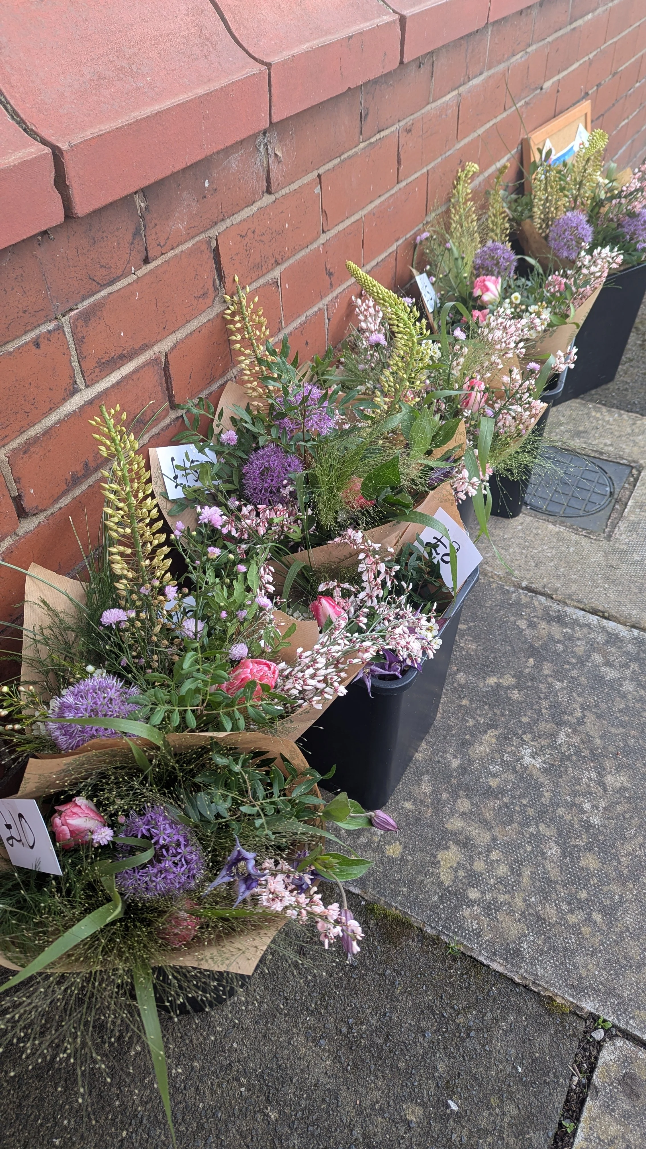 Colourful flower bouquets from the Leftover Flower Club lined up against a brick wall on the pavement.