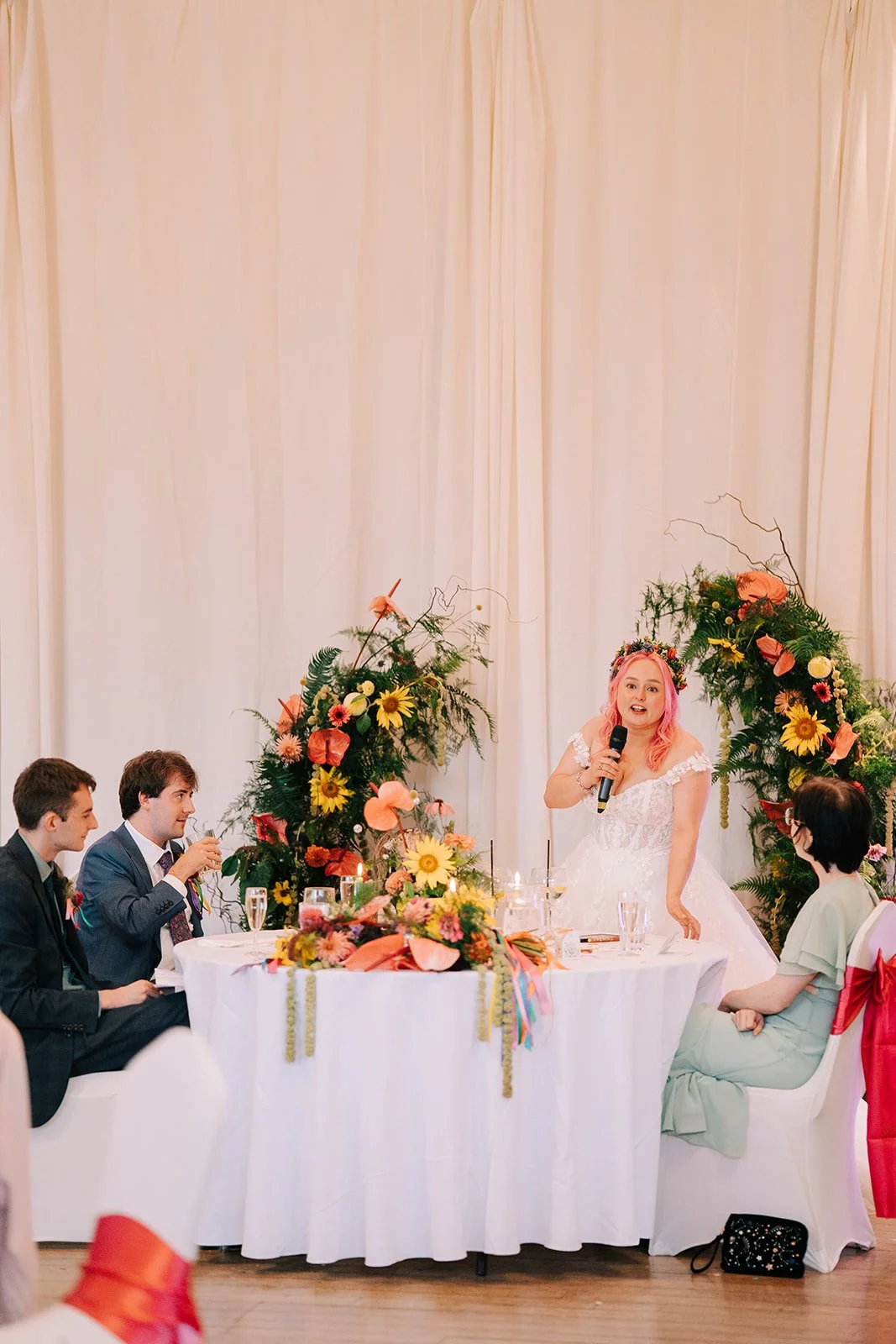 Bride giving a speech in front of colourful wedding split arch created by MillieBuds Colour Loving Wedding Florist in Stockport at Bowdon Rooms