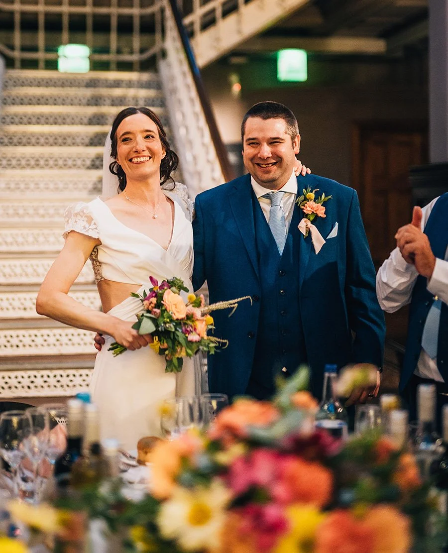 Couple arrival at wedding breakfast behind bright colourful wedding flowers