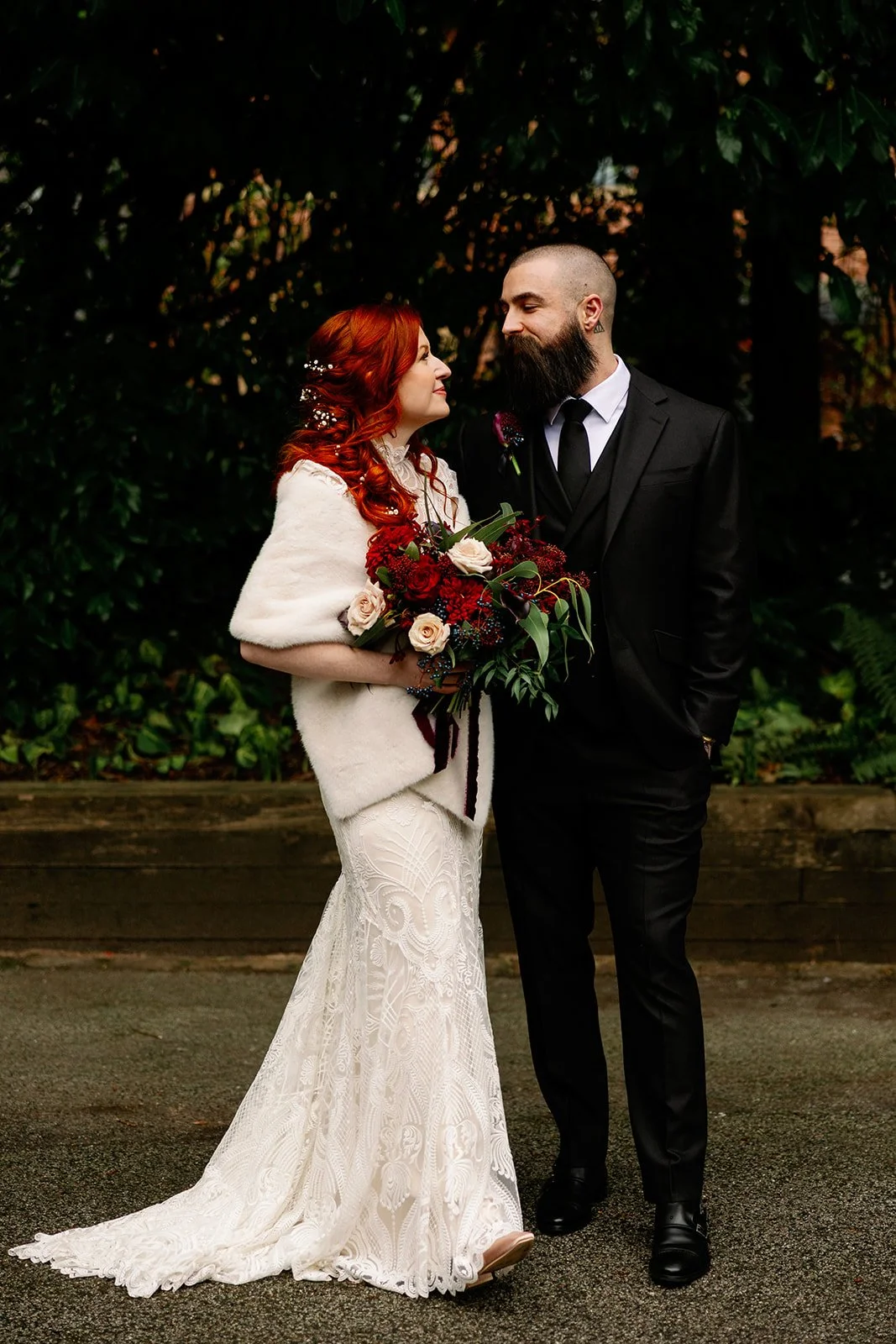 Bride and groom posing with an abundant moody red bouquet created by MillieBuds Wedding Florist, Stockport